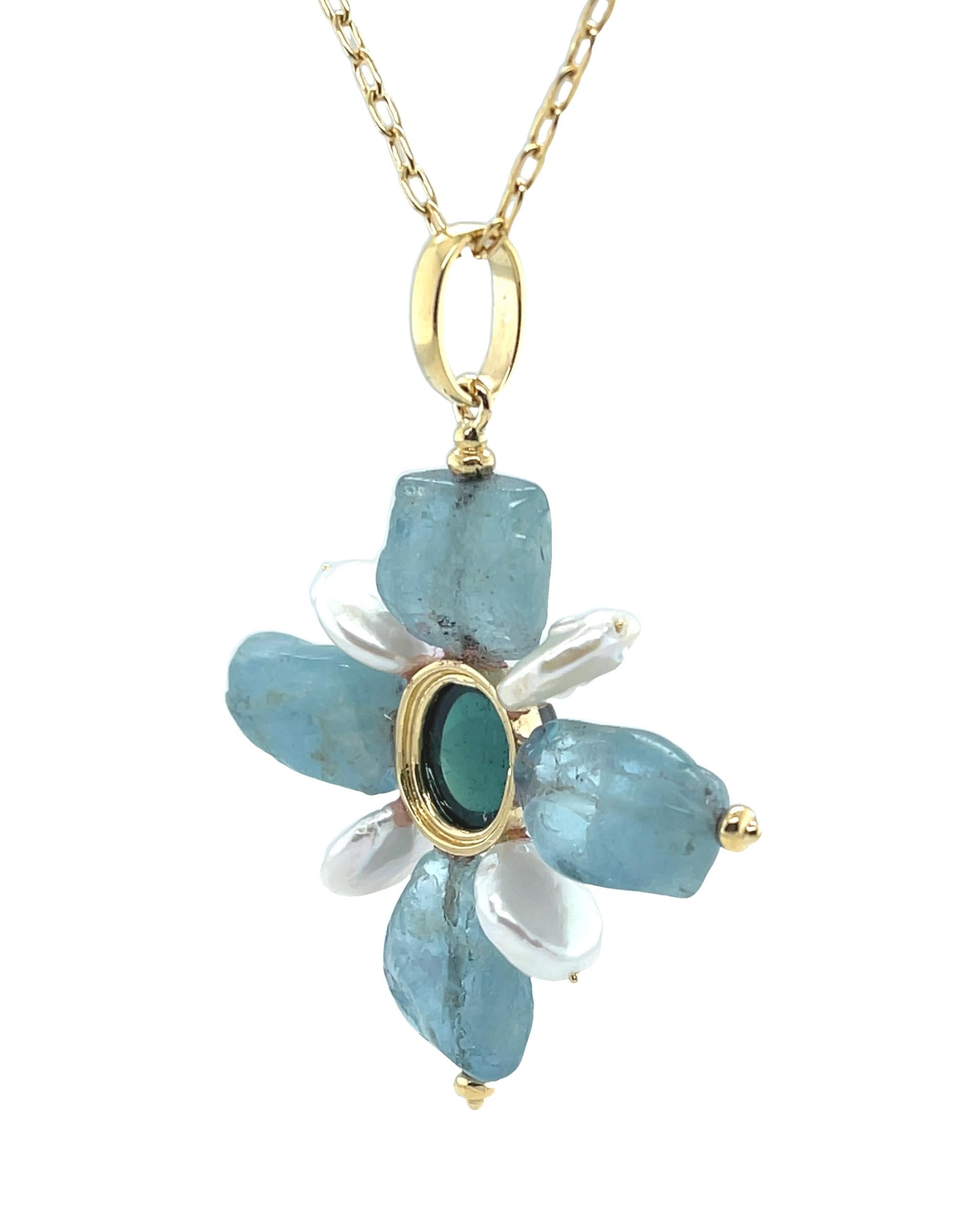 This eye-catching cross pendant features deep blue aquamarine freeform beads and white coin pearls arranged around a beautiful indicolite tourmaline cabochon. The indicolite tourmaline is a rich shade of teal greenish blue, and bezel set in bright,