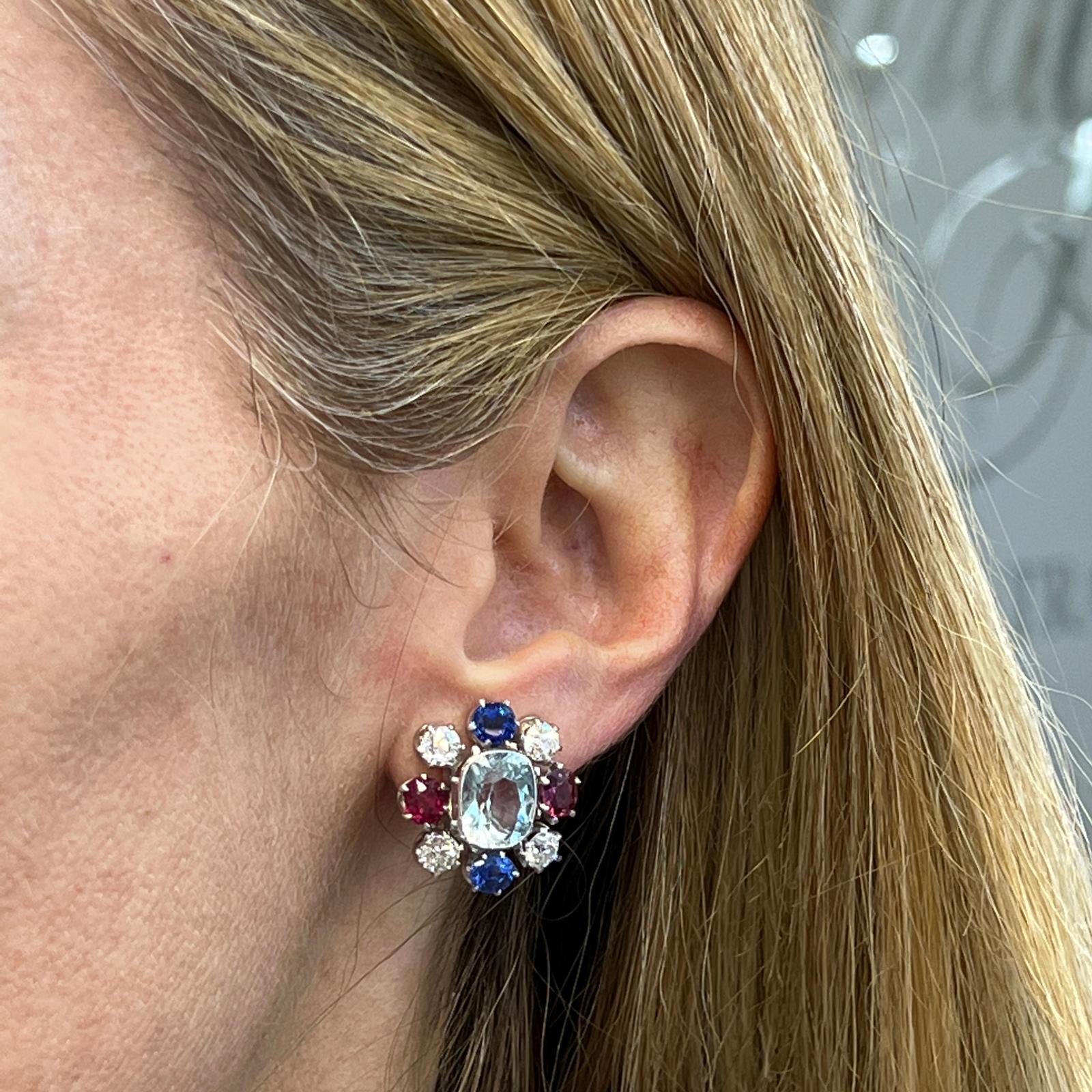Fabulous and beautifully preserved aquamarine, diamond, ruby, and sapphire earrings fashioned in 14 karat white gold. These turn of the century earrings feature 2 oval aquamarine gemstones weighing approximately 6.00 CTW. The aquamarines are bezel