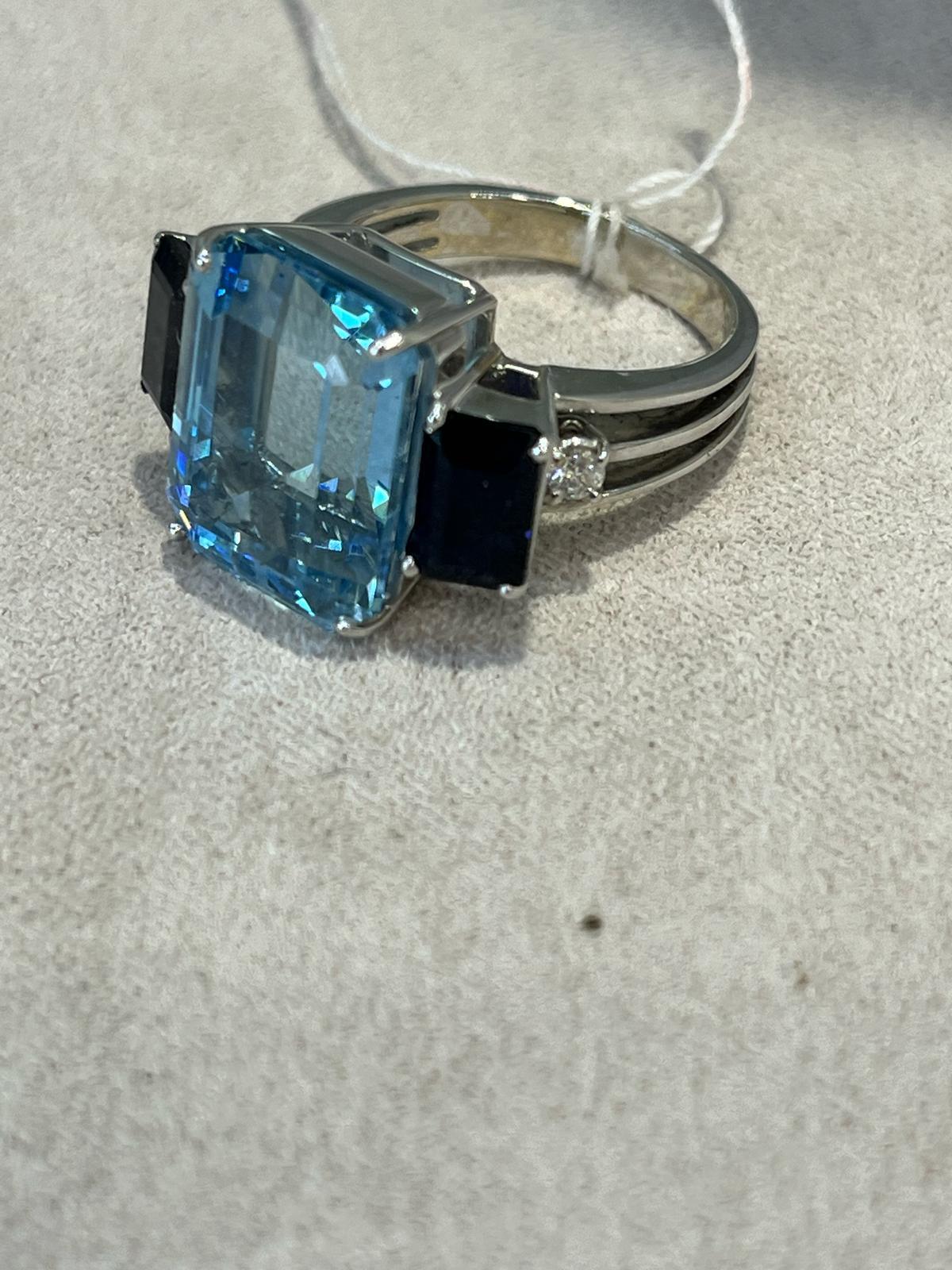 Anello in oro con pietre di acquamarina e zaffiro incastonate
Marchio: Antonini 
Materiale: oro bianco 18 carati

Pietra centrale: Acquamarina
Taglio: Taglio smeraldo
Peso: 12 carati

Pietre laterali: 2 zaffiri
Taglio: Taglio smeraldo
Peso totale: 2