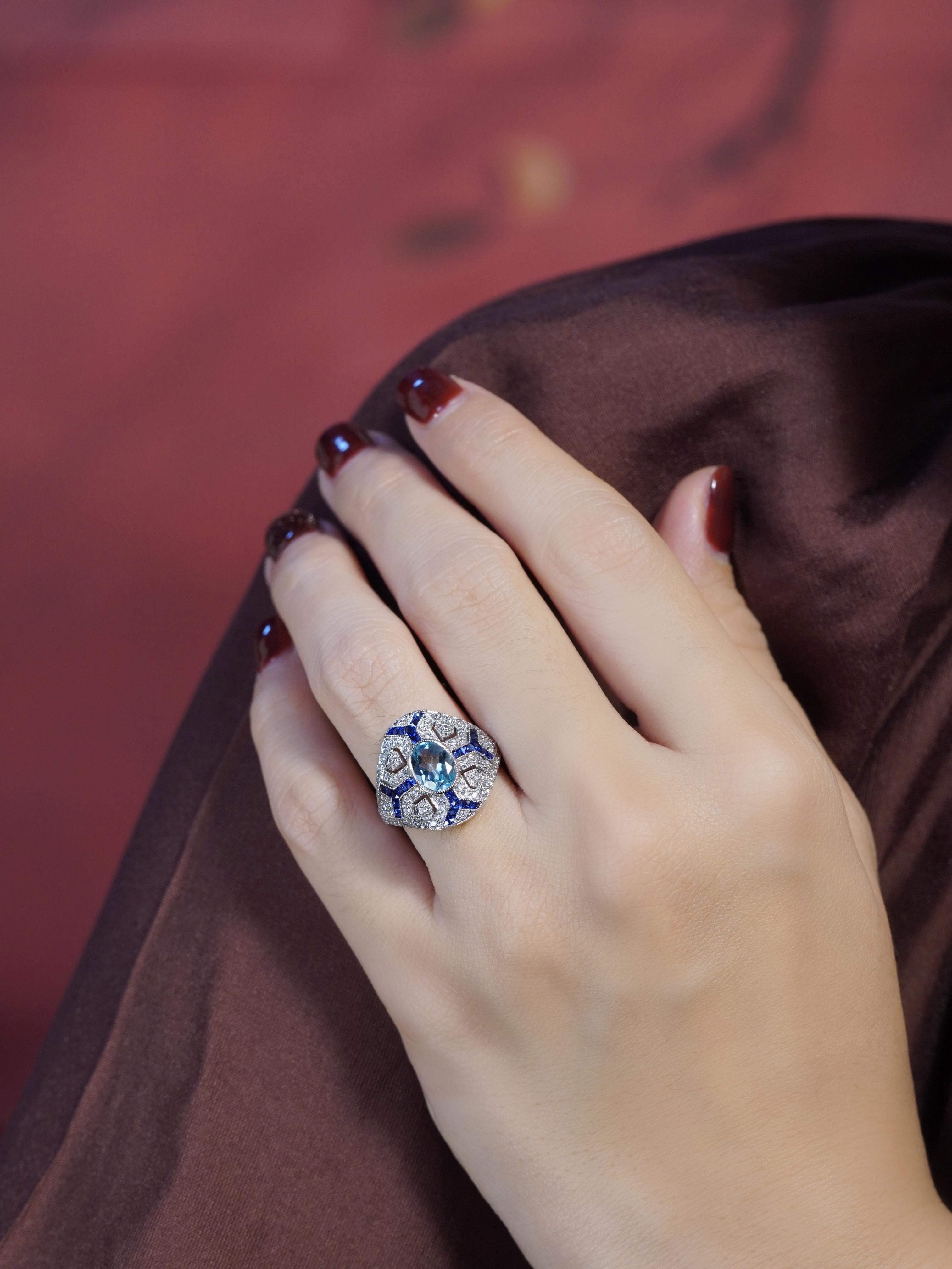 A  atemberaubender ovaler Aquamarin, gefasst in einer sicheren Lünettenfassung. Die Vorderseite des Rings ist mit zarten Linien aus Diamanten und Saphiren geschmückt, die sich von jeder Ecke aus elegant auffächern und ein auffälliges geometrisches