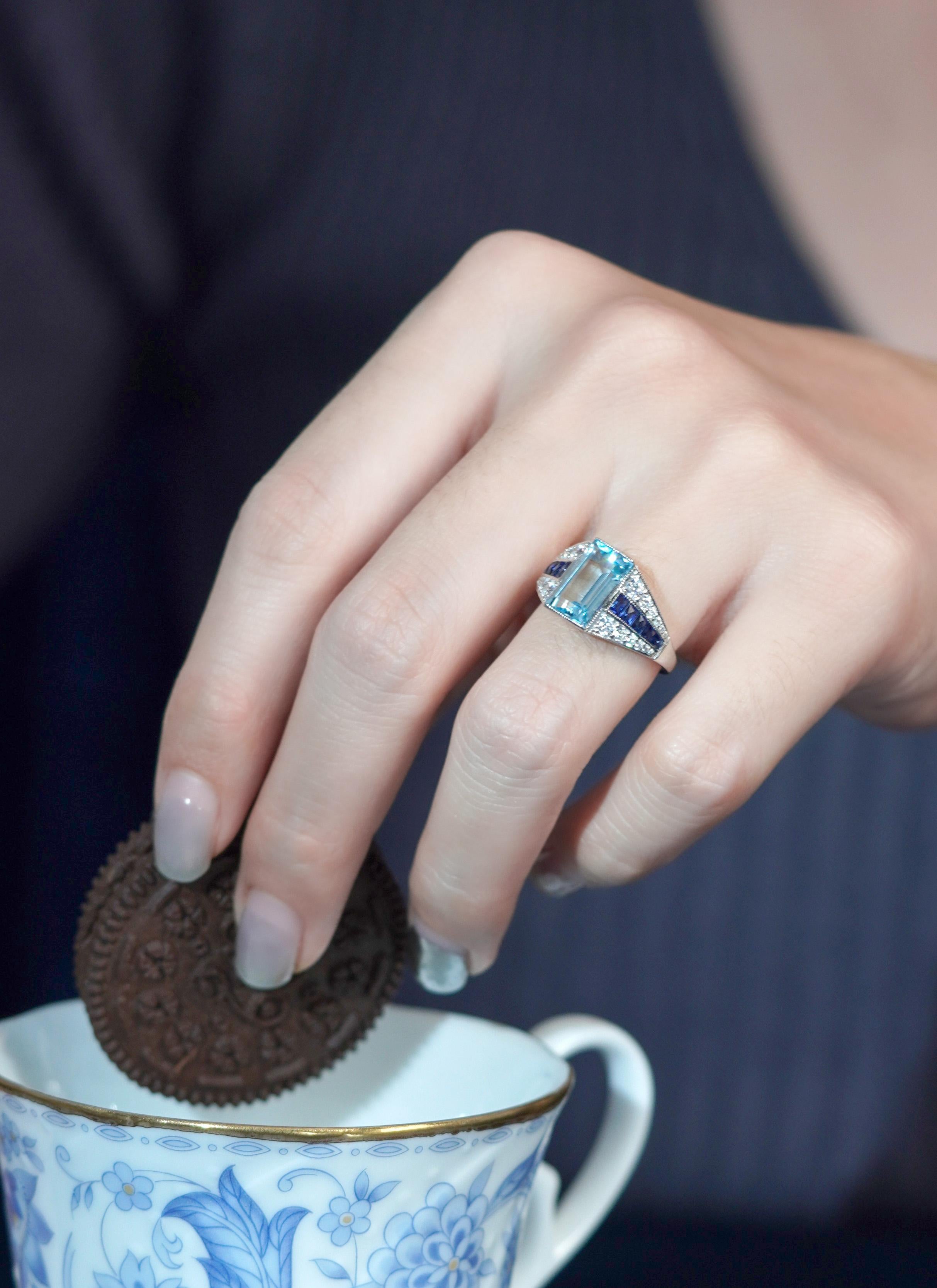 Cette magnifique bague de fiançailles de style Art déco, où la sérénité de l'aigue-marine rencontre l'allure vibrante du saphir bleu. La pièce centrale en aigue-marine est magnifiquement complétée par des diamants éblouissants qui ornent les deux
