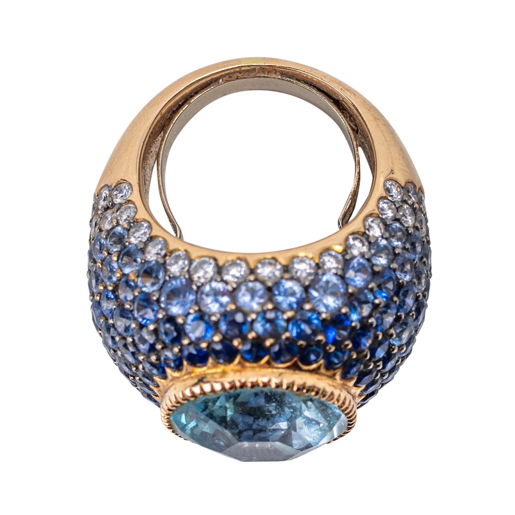 Aquamarin, Saphir und Diamant Bombé Ring aus 18K Gelbgold

Ein aufsehenerregender Kuppelring aus 18 Karat Gelbgold mit einem großen ovalen Aquamarin von ca. 10 Karat in der Mitte, umrahmt von einem nahtlosen Pavé aus abgestuften blauen Saphiren, die