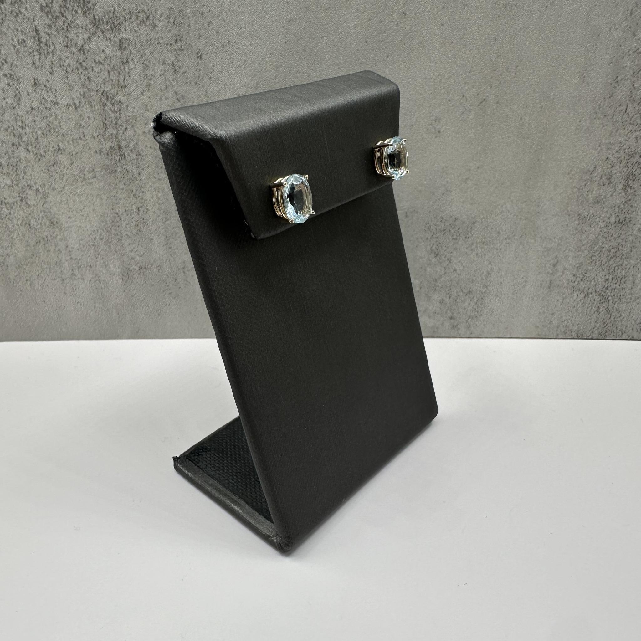 Ces élégantes boucles d'oreilles en or jaune 14kt sont composées d'aigues-marines ovales d'un poids total de 3,21 carats, serties dans des montures panier classiques à 4 branches. Le bleu serein des aigues-marines contraste magnifiquement avec la