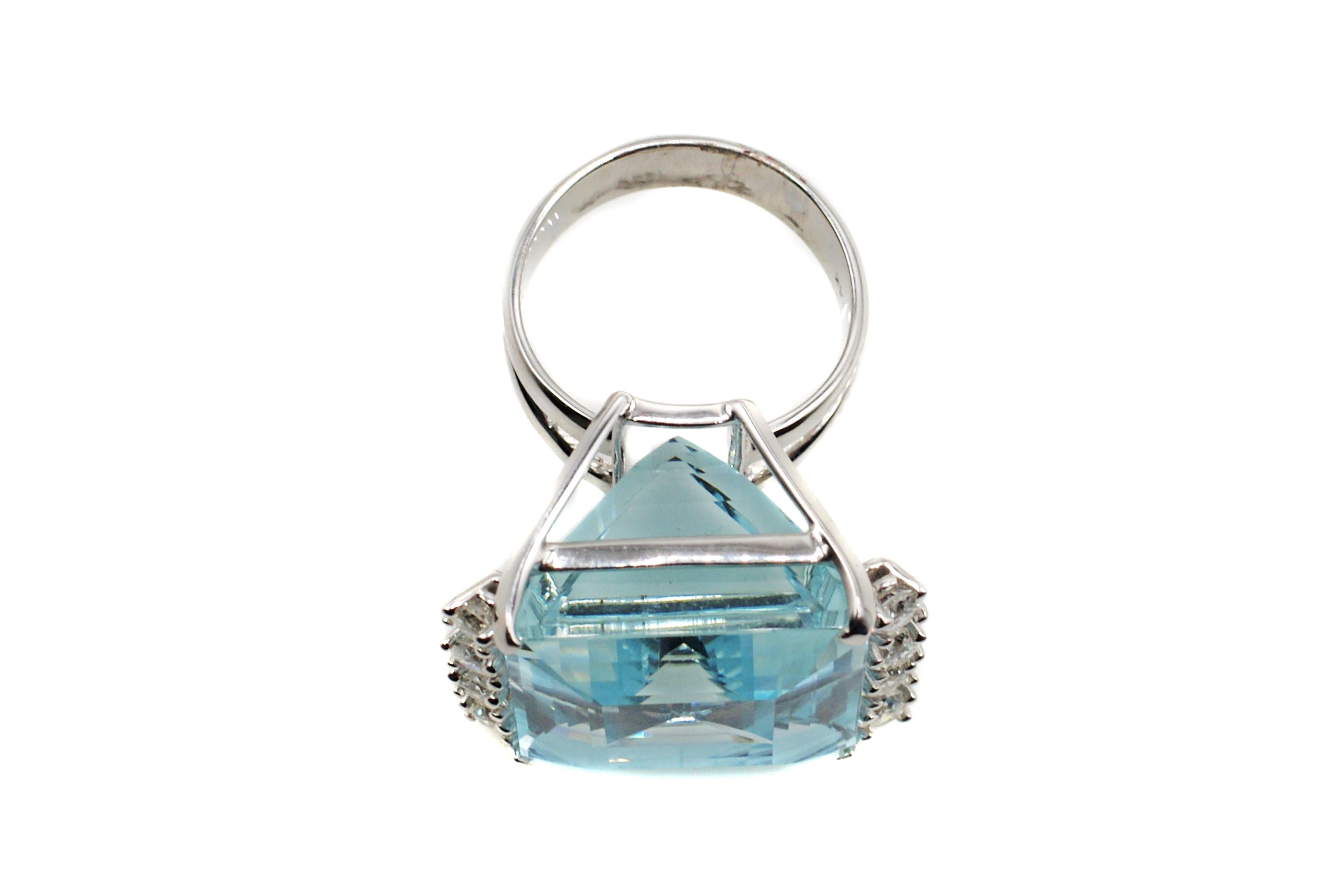 This bold ring shows off a perfectly square step-cut Aquamarine measured to weigh approximately 35 carats. The lively pastel-blue center gem is set with 4 prongs and is embellished by 4 bright white and sparkly brilliant cut diamonds on either side.
