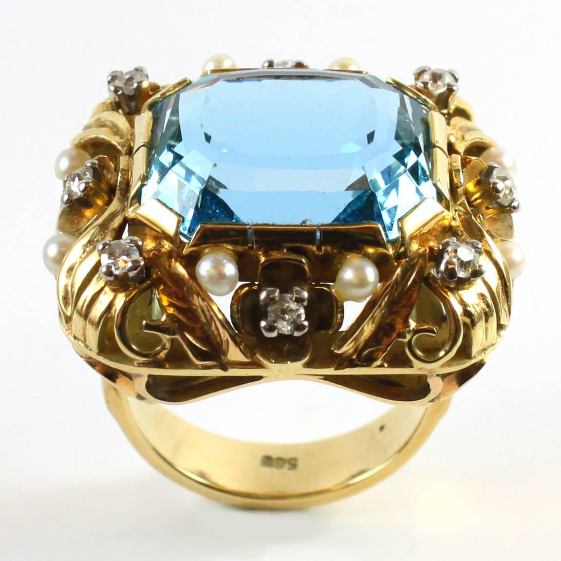 A aquamarine, pearl and diamond ring in a floral design in yellow gold from the Retro period, 1940s. The ring centres a big aquamarine, ca. 16 carats and it is accentuated by round brilliant cut diamonds and pearls.