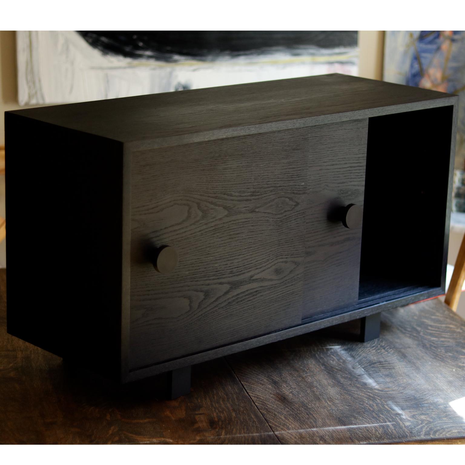 Der Aquinas-Schrank ist ein kompakter Schiebetürenschrank, der sich perfekt für Schallplatten, Bücher und kleinere Gegenstände eignet. Dieser minimalistisch gestaltete Schrank mit handgefertigten schwedischen Beschlägen ist für die leichte