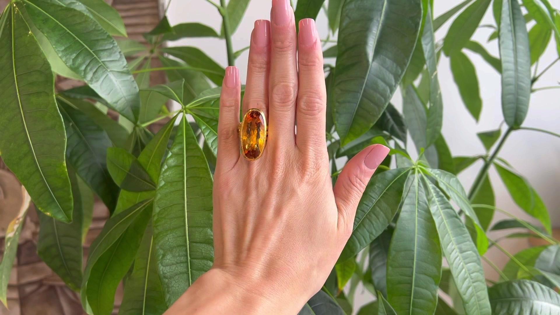One ARA 21.15 Carat Citrine 24 Karat Yellow Gold Cocktail Ring. Featuring one oval faceted golden citrine weighing approximately 21.15 carats. Accented by 11 round brilliant cut golden citrine with a total weight of approximately 1.00 carat. Crafted