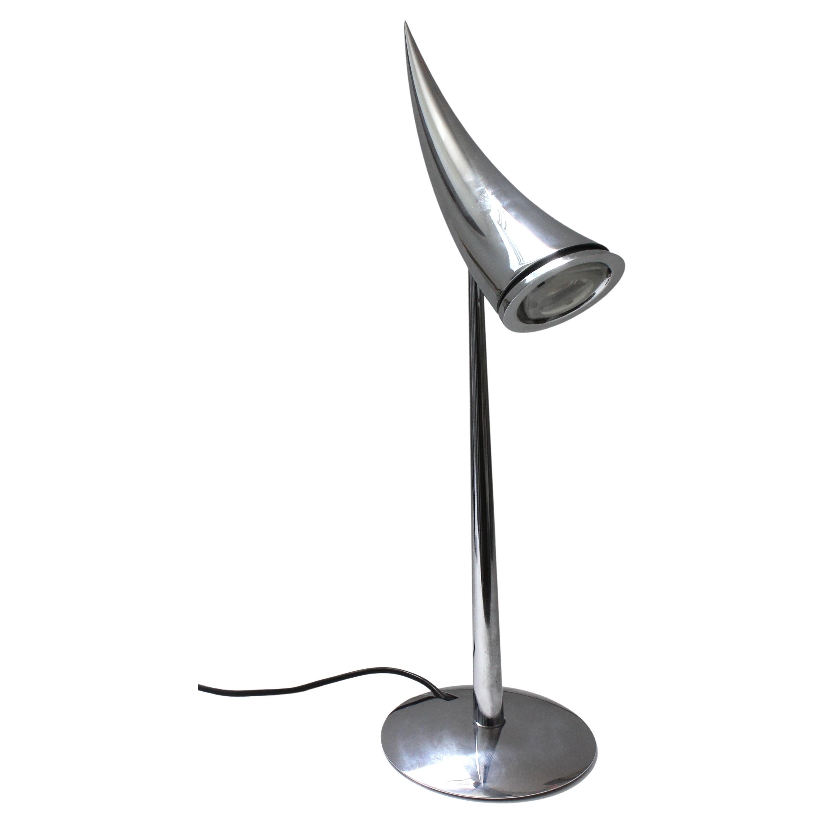 This stylish, polished steel table lamp is known as the Ara, and it was created in 1988 by Philippe Starck for Flos.

The lead image shows the lamp in its off position (with the tip of the cornucopia downward) and you need to grab the horn and