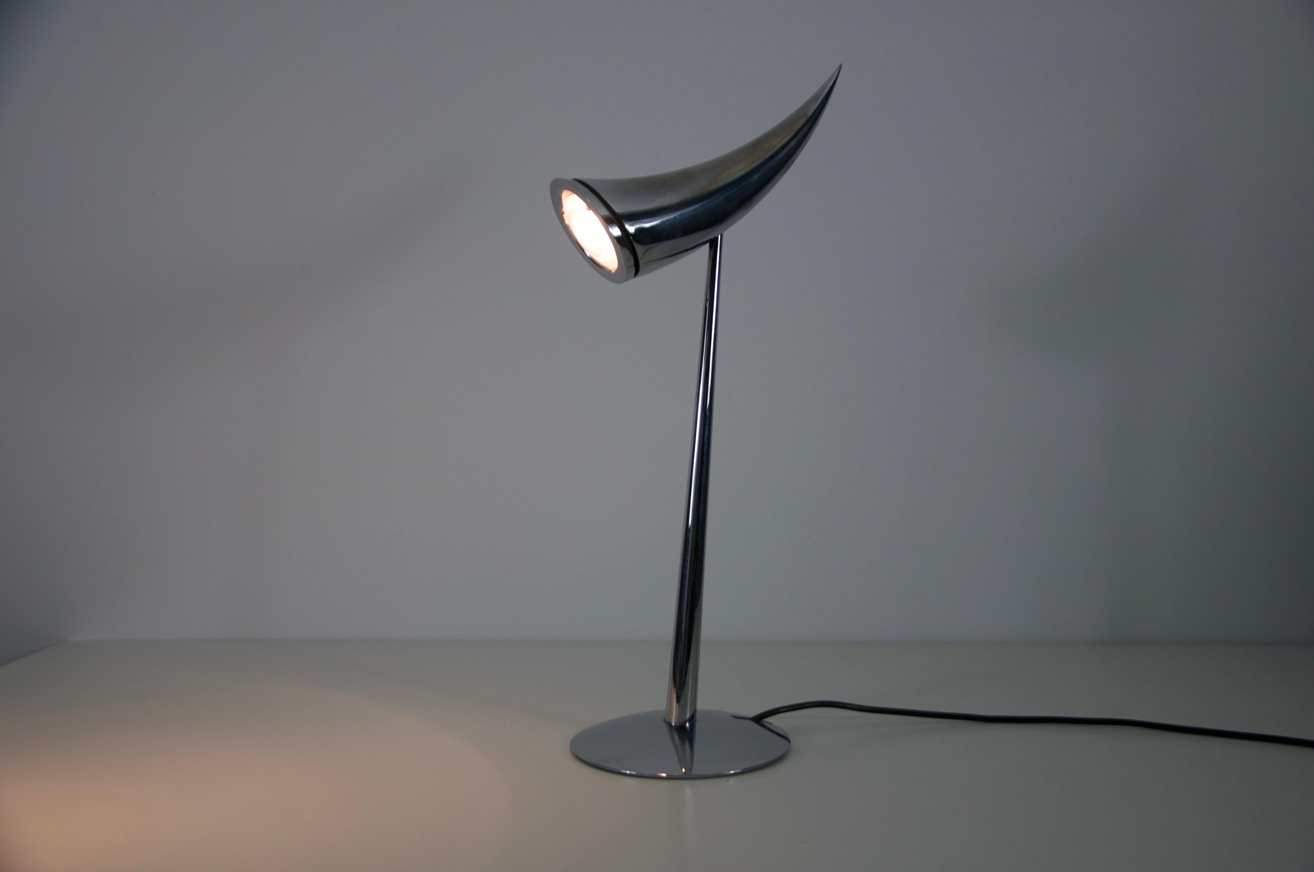 La lámpara de sobremesa Ara fue diseñada por Philippe Starck para Flos en 1988 y es un sorprendente ejemplo de diseño de iluminación posmoderno. Con su silueta elegante y minimalista y su acabado en cromo pulido, la lámpara se asemeja a un cuerno