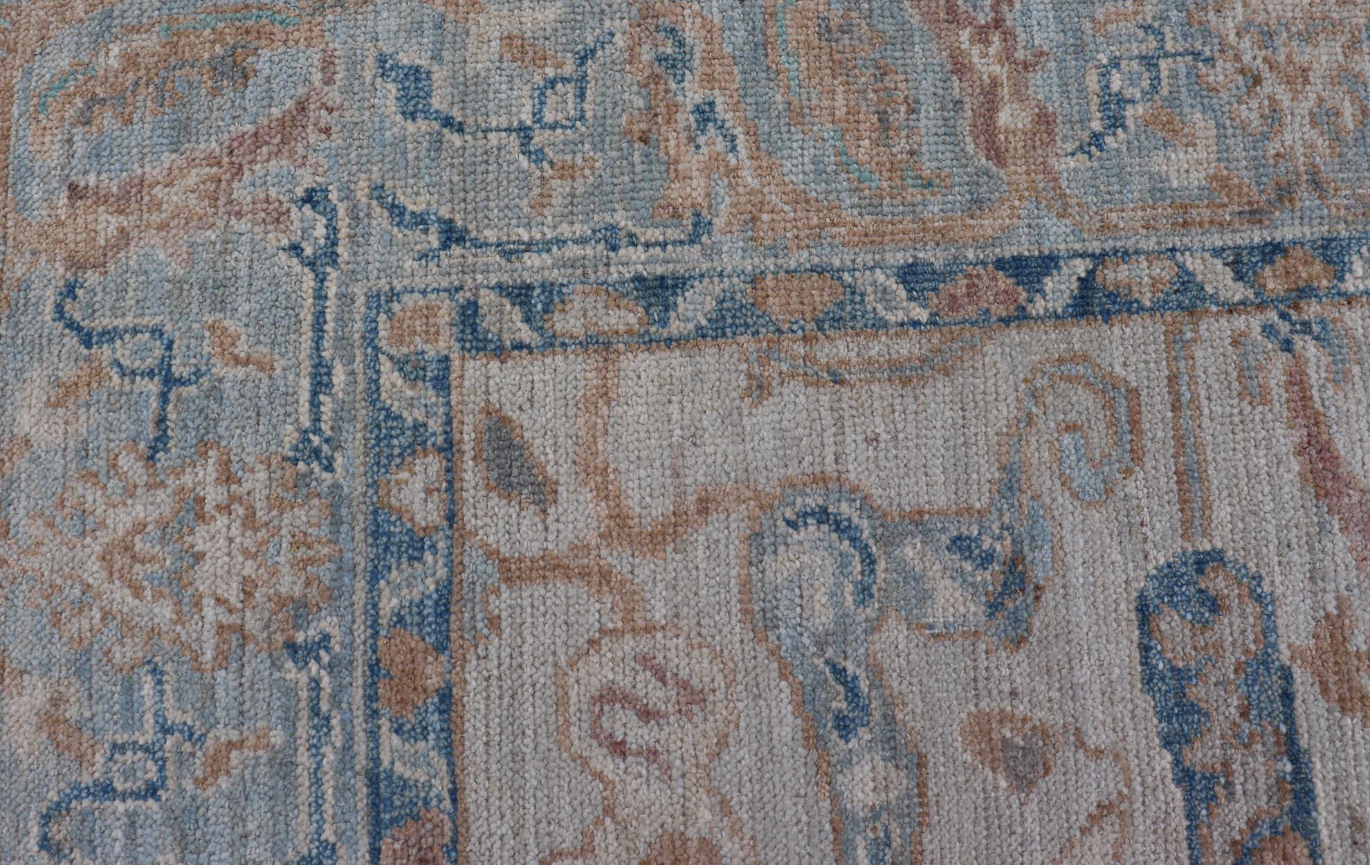 Hand knotted Oushak made of wool. The field is backed by a ivory color, with a light blue border, etched with elegant golden/brown branches. The arabesque-like design brings splashes of light blue, cognac, and reddish brown color. 
Measures; 5'1 x