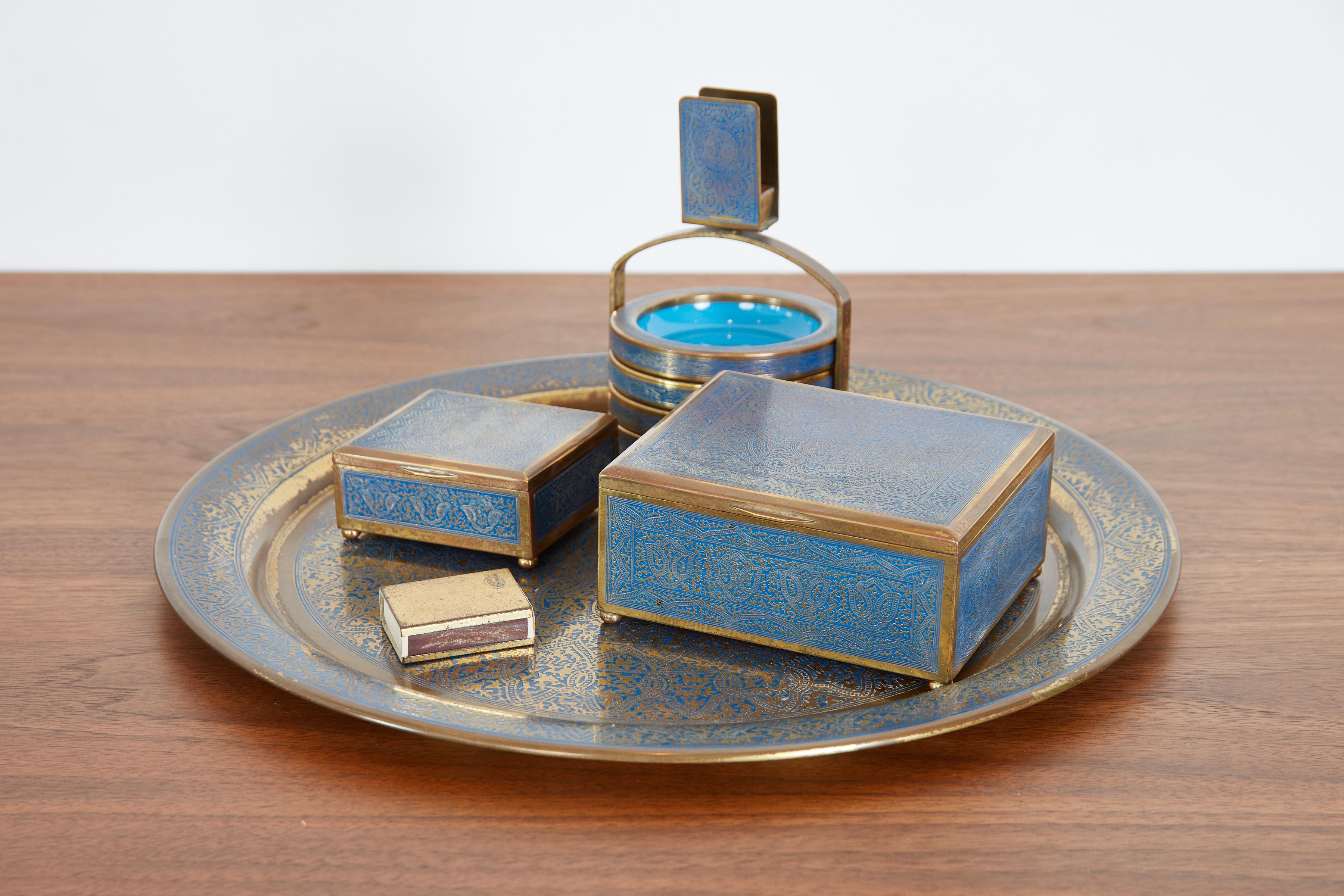 Incredible varnished brass Morrocan tea and smoking set. 
Marrakesh, 1970s 
Set consists of a gold and blue round tray, four colorful enameled coasters or ashtrays, with its object to carry them, a lighter, a cigar holder with matchbox, and a tea