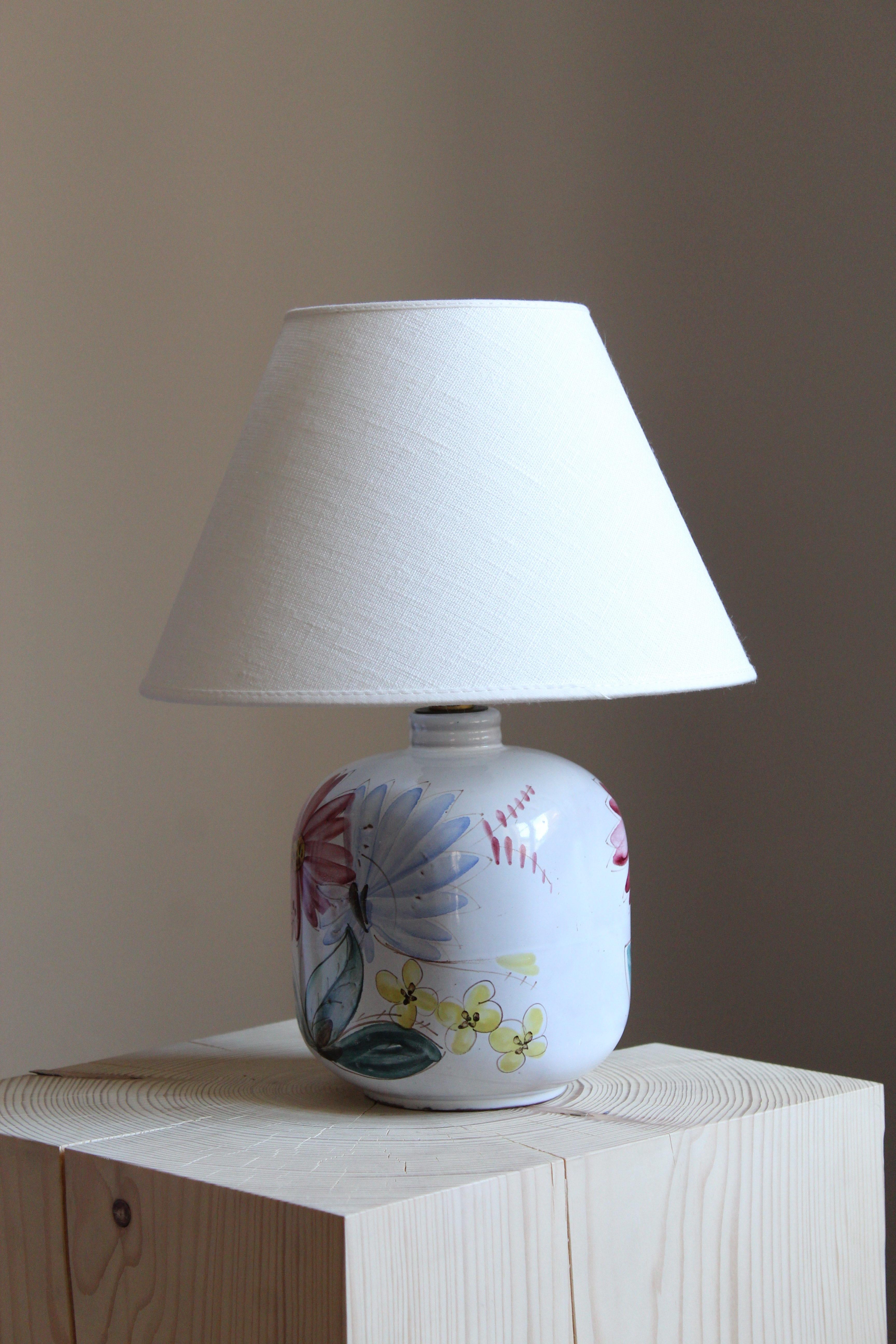 A table lamp. Designed and produced by Arabia, Finland, 1960s. In stoneware or earthenware. Glazed and painted. Lampshade not included.

Glaze features white-red-green-blue-yellow colors.