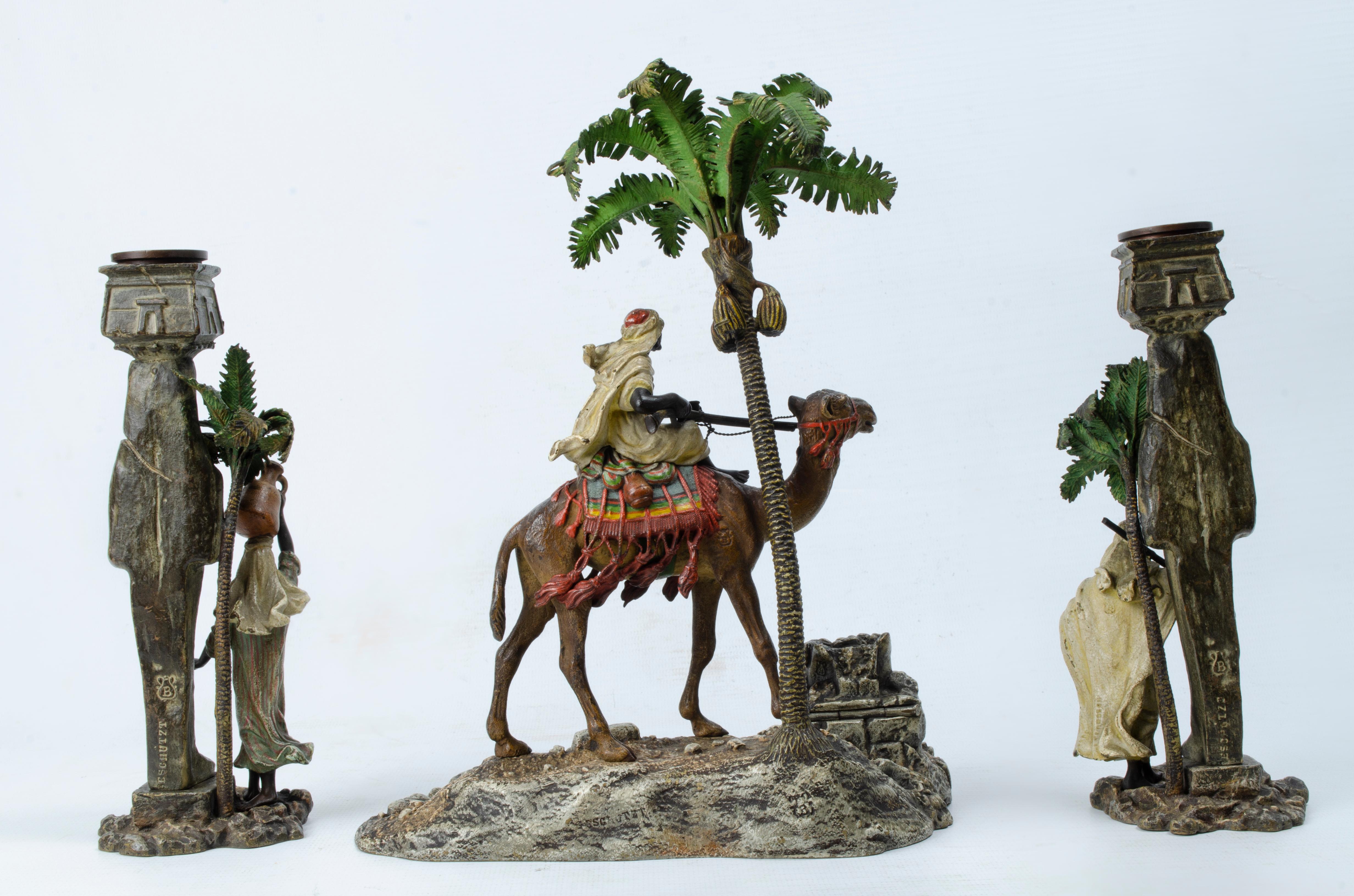 Arabische Themengarnitur von Franz Xavier Bergman (1861-1936). Die Stücke sind aus polychromer Bronze gefertigt. Im Mittelpunkt stehen ein Tintenfass, das zwischen den Felsen versteckt ist, und ein arabischer Krieger, der auf einem Kamel neben einer
