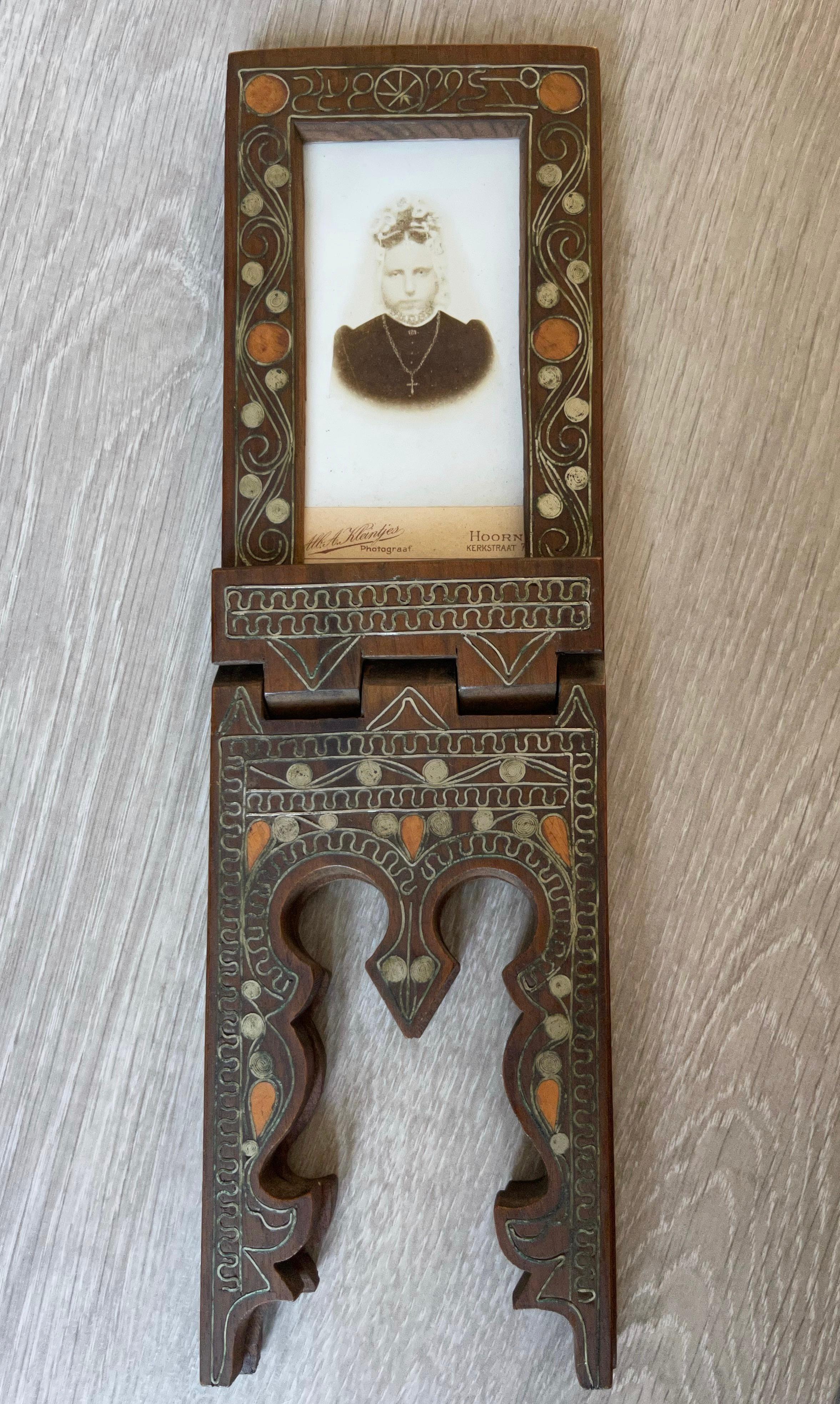 Handcrafted of one piece of solid wood, inlaid with silver, scrolling, decorative picture frame.

This picture frame is easy to fold into a cross legged standing position and this rare example is inlaid with silver motifs and a glass-like red