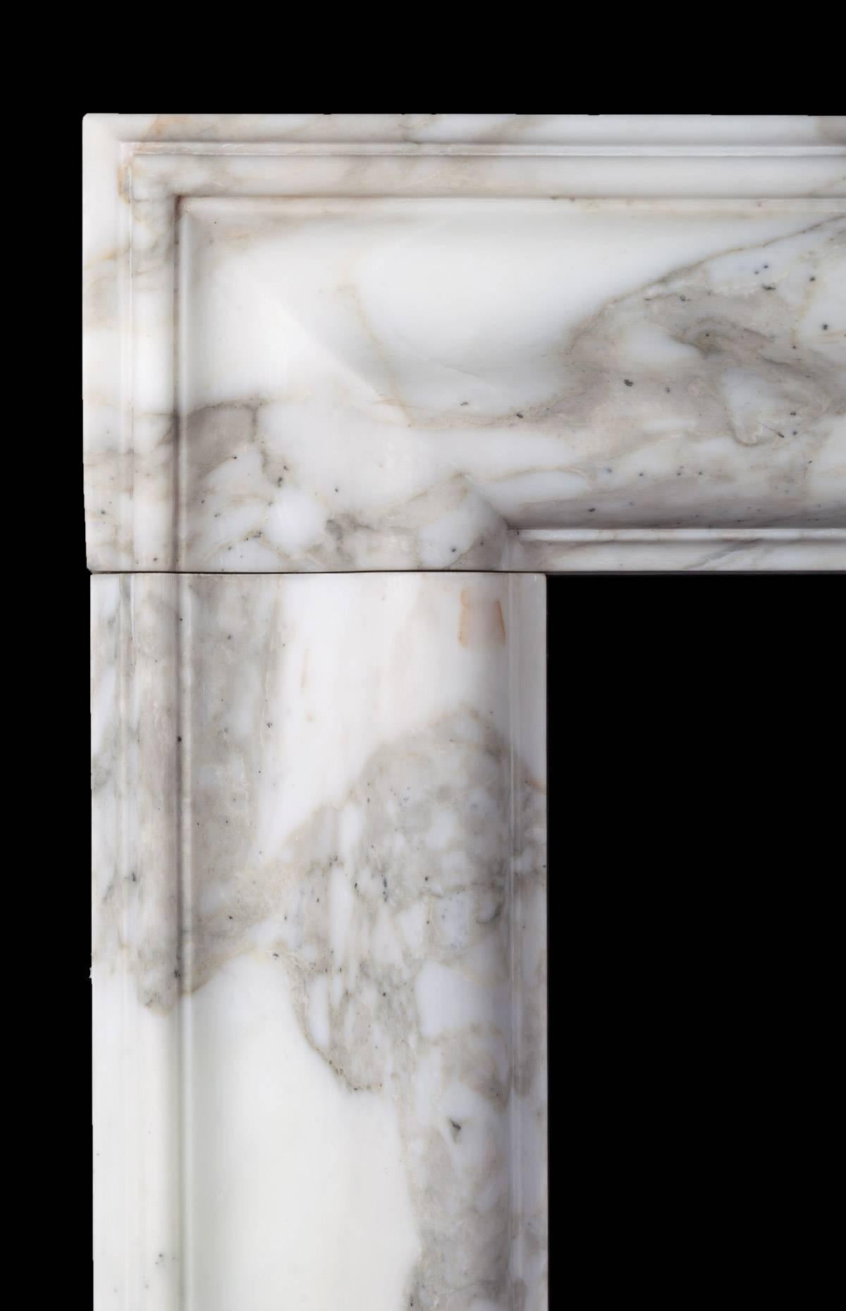 A classic bolection fireplace with moulded frame on plain square plinths, carved from three solid pieces of marble with mason mitred corners. Made by Ryan & Smith from a beautiful block of Arabscato Carrara marble sourced in Italy.