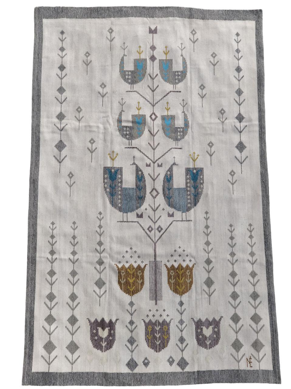 Kilim (arazzo) tessuto a mano in lana. Disegno su fondo chiaro che rappresenta uccelli e tulipani stilizzati, con colori tenui sul celeste e marrone. In basso a destra il monogramma del nome dell’artista N E - Eva Nemeth.  Tessuto a mano nel