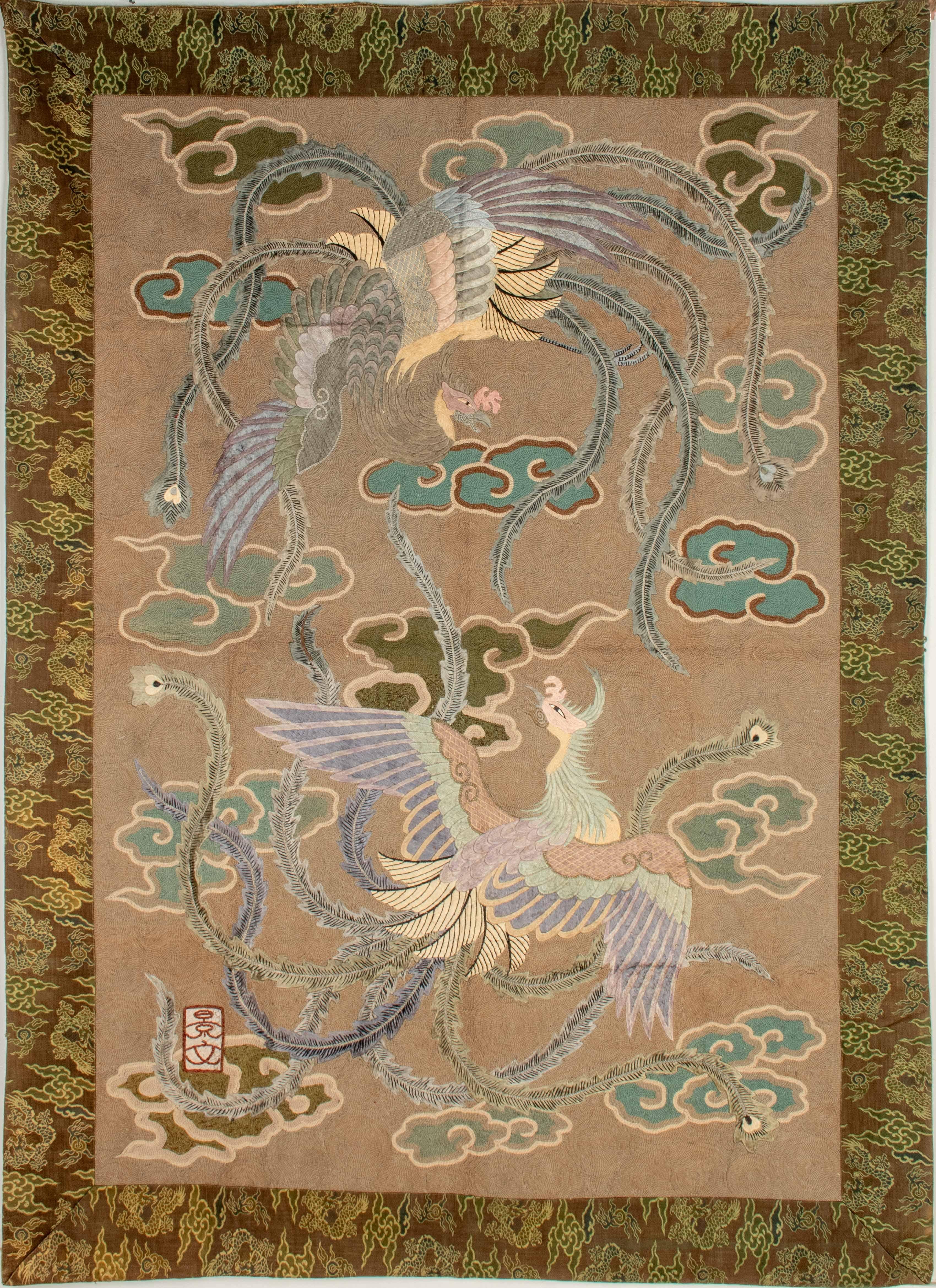 Fein mit polychromen Fäden reliefartig bestickter Seidentapisserie mit einem pastellfarbenen Phönixpaar in der Mitte auf sandfarbenem Grund, zwischen stilisierten Wolkenvoluten.

Die gesamte Szene ist von einem Rahmen umgeben, der mit gestickten