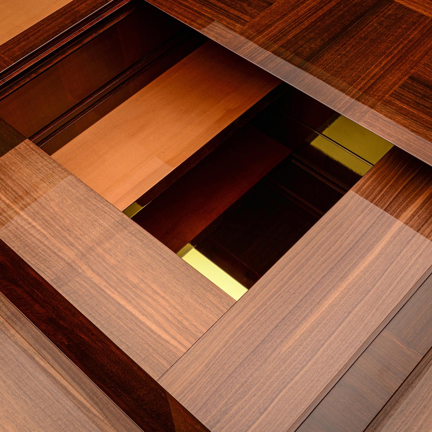 La table basse Arcano de Storagemilano se compose d'un cube compact en bois plaqué d'eucalyptus très brillant, avec des étagères coulissantes et des compartiments cachés. Les étagères intérieures en noyer italien, noyer Canaletto et érable offrent