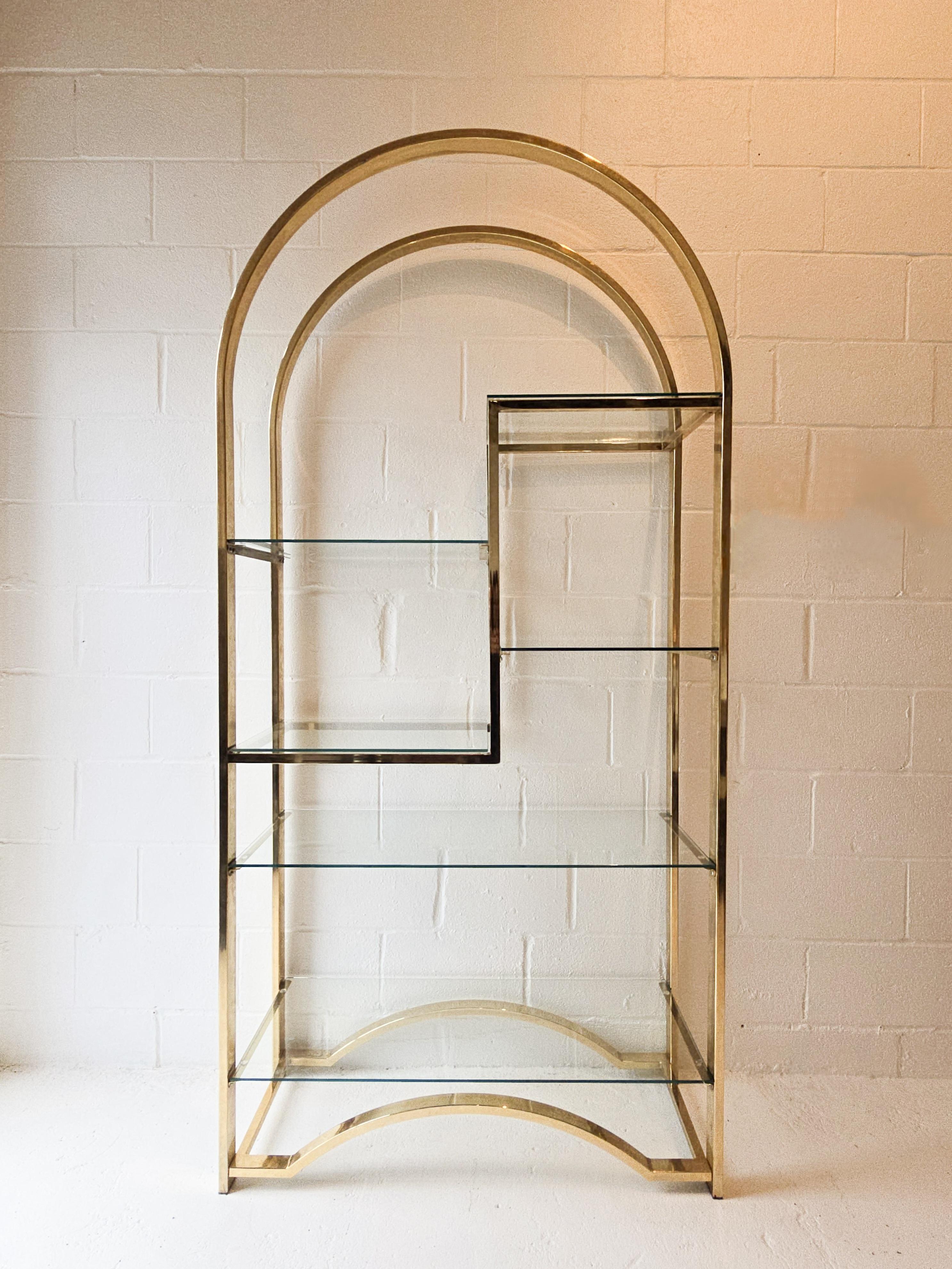 Impresionante etagere de latón y cristal. Este etagere tiene un marco de latón con una tapa en arco y estantes de cristal de distintos tamaños. El cuerpo de latón está bien elaborado. Hay seis estantes de cristal, tres de los cuales son 