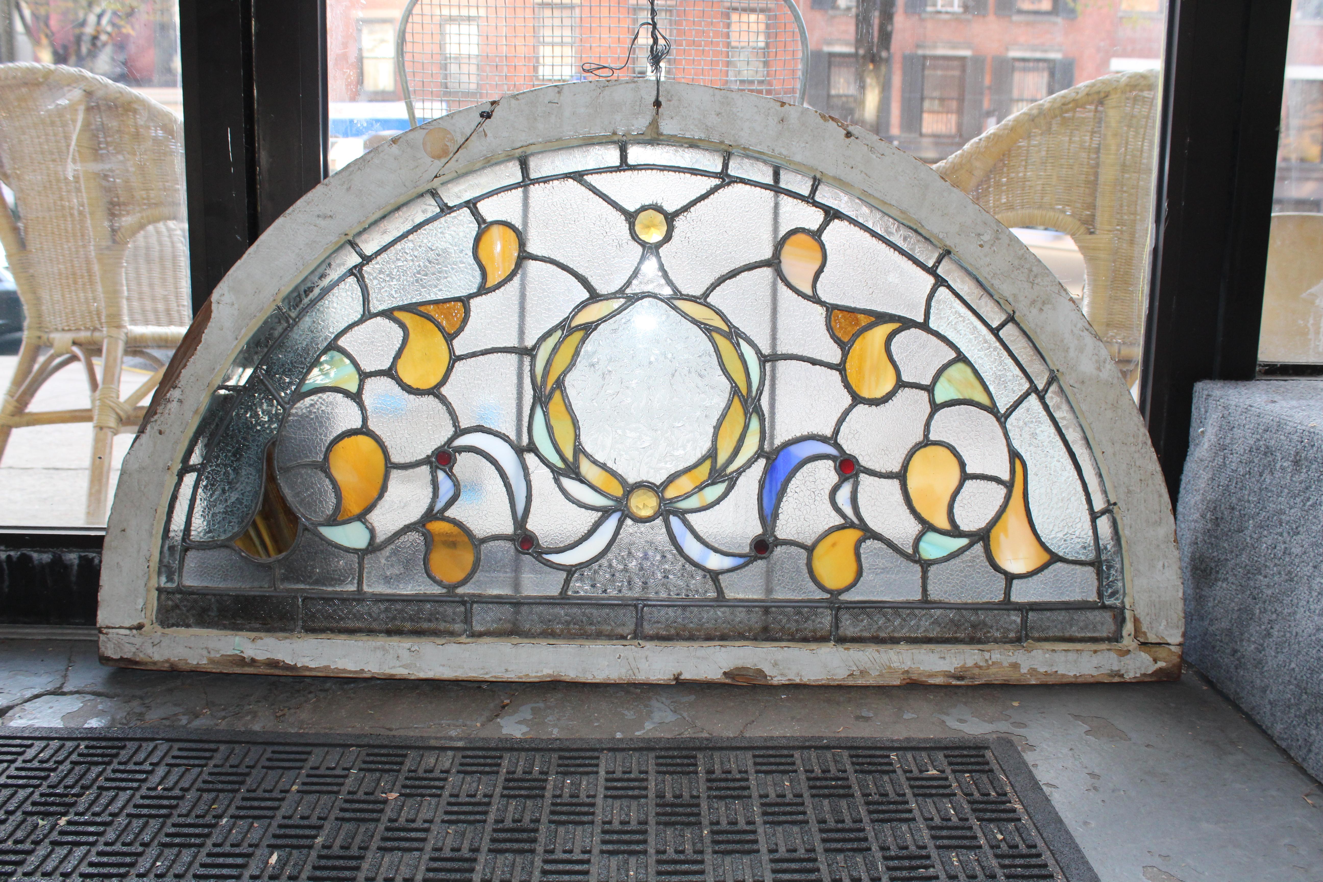 Antique arch window for over your doorway with stained glass designs. Clear textured glass gives privacy while letting ample light in. Colorful designs surround the center wreath. 
Currently housed in a wooden frame - the overall dimensions are for