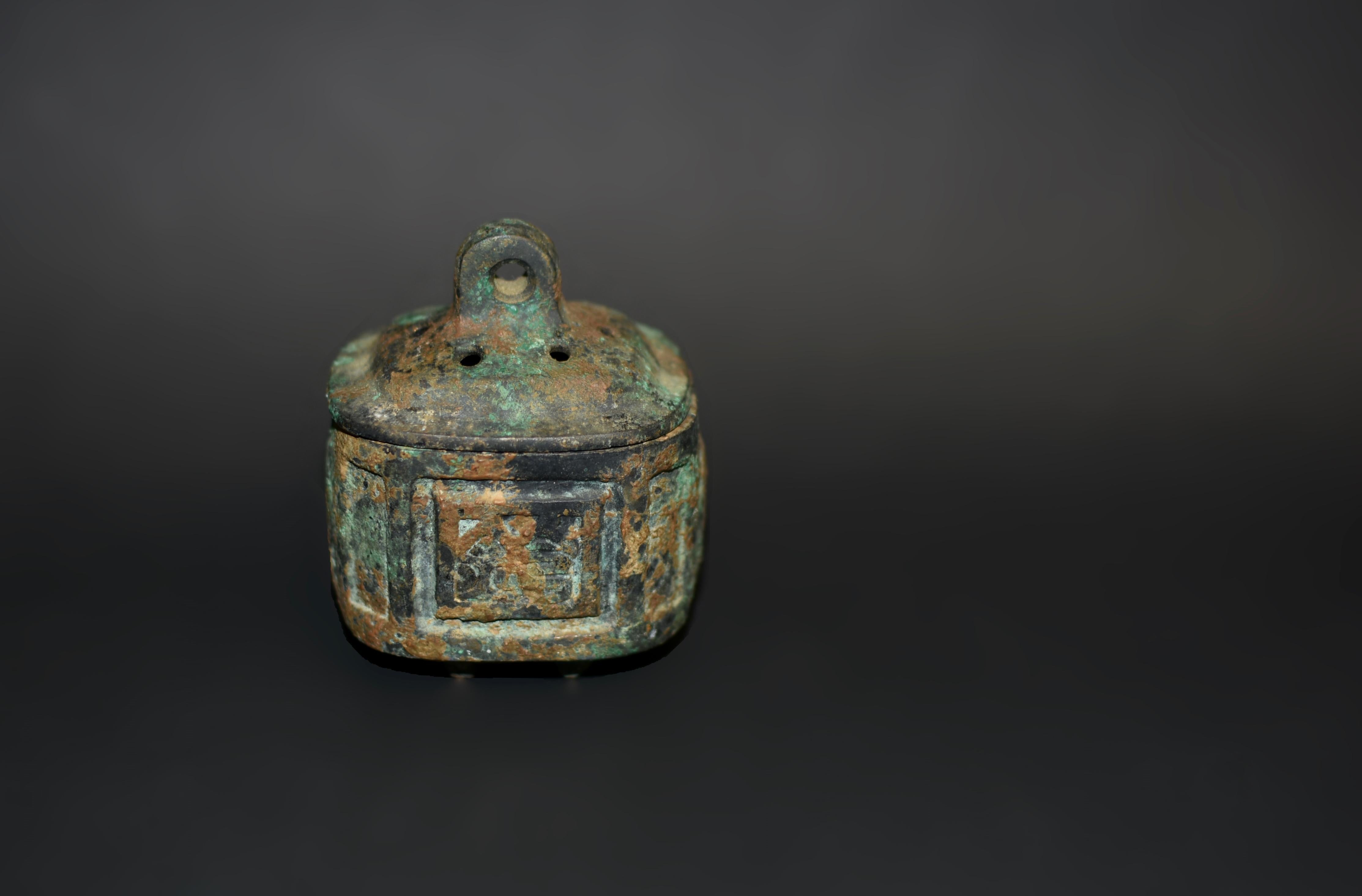 A small rare archaistic Chinese bronze censer. Raised on four tiny feet, the rectangle form with chamfered corners, both sides featuring what appear to be stylized dragons within squares in the center, the fitted cover with six pierced apertures