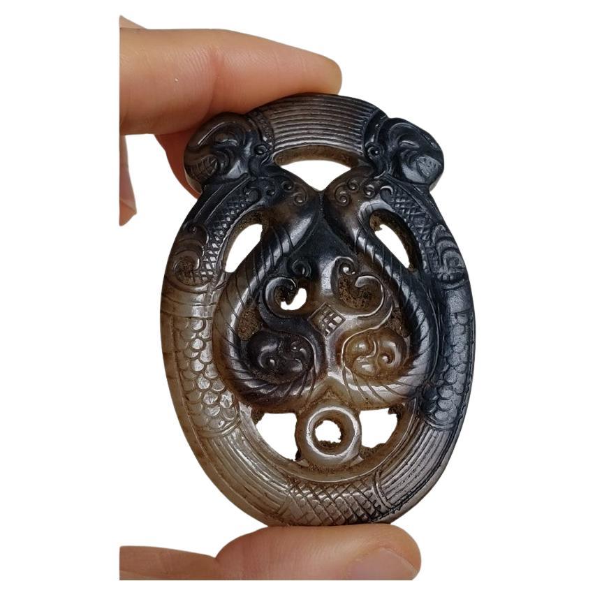 Ce pendentif en jade archaïque présente un motif symétrique avec deux chilong dont les corps serpentins forment un cœur. 

Au sommet se trouvent deux têtes de chilong, souriantes et regardant dans des directions opposées. Le corps du chilong est