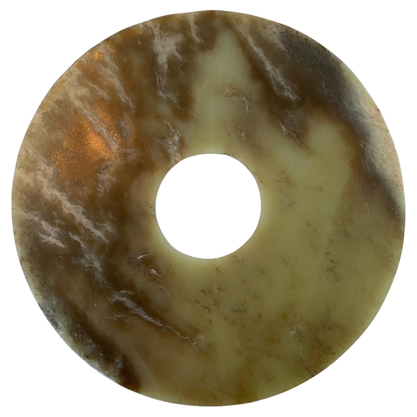 Bi en jade vert et brun translucide de la dynastie Zhou (1046 C.I.C. à 256 C.I.C.). Les formes organiques créées par le mélange de ces deux couleurs principales évoquent la beauté d'une flamme, tandis que les éclats occasionnels de blanc donnent de