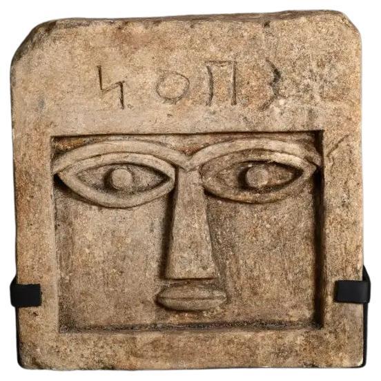 Questa stele in pietra arenaria, modello Arcades, è una scultura decorativa realizzata a mano e ispirata all'arte sud-araba dell'antico Yemen. Risalente stilisticamente al III-I secolo a.C., presenta un volto umano stilizzato con sopracciglia