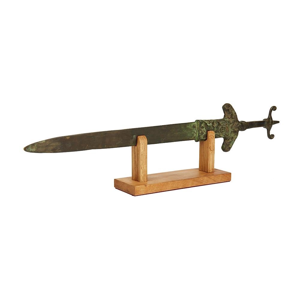 A stylish and interesting archaic styled bronze sword with integral antenna shaped handle with native figures with dogs molded in relief to both sides of the hilt and with a green verdigris patina with heightened naturally polished elements. 

The