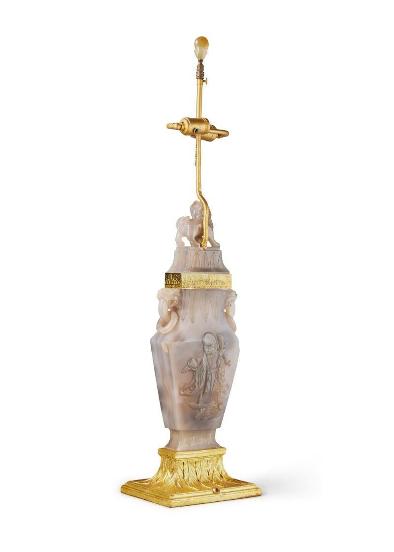 Our beautiful carved agate in archaistic urn-form features the figures of a wise man and female dancer and was mounted as a lamp in the early 20th century. It is mounted on a carved giltwood base and has hand-hammered gilt metal mounts and luxurious