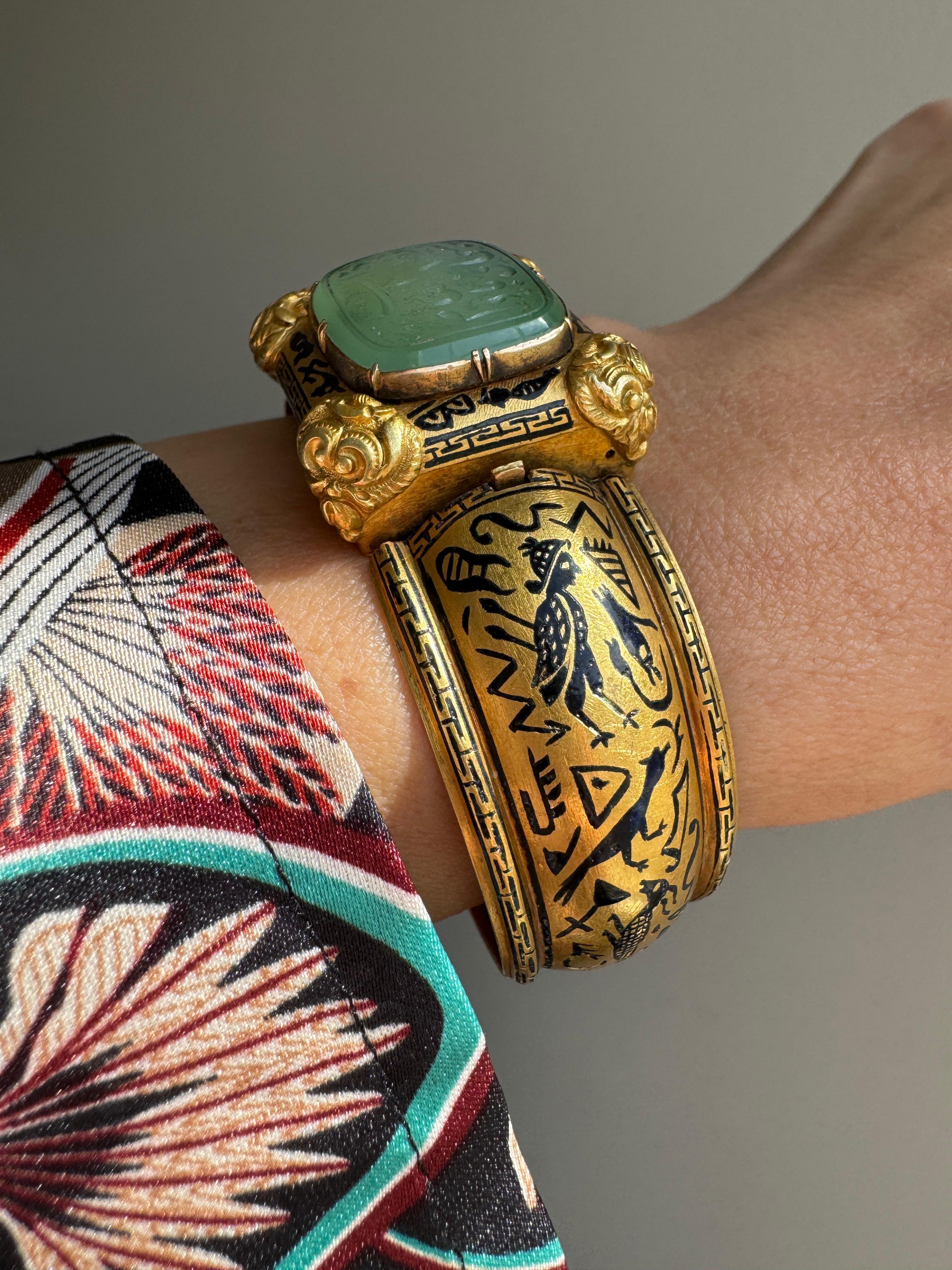 This exquisite  archeological-revival bangle is attributed to Robert Phillips, circa 1865. The hinged bangle is decorated with Egyptian hieroglyphs in glossy black enamel culminating in a jade intaglio with a covered compartment to the reverse. 