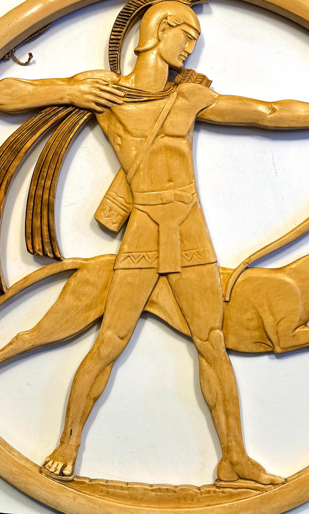 Large and impressive, this high style Art Deco wall sculpture by New Art Wares depicts a muscled Greek warrior readying his bow for the shot, accompanied by a greyhound racing toward their target. The painted plaster relief is sharp and chiseled,