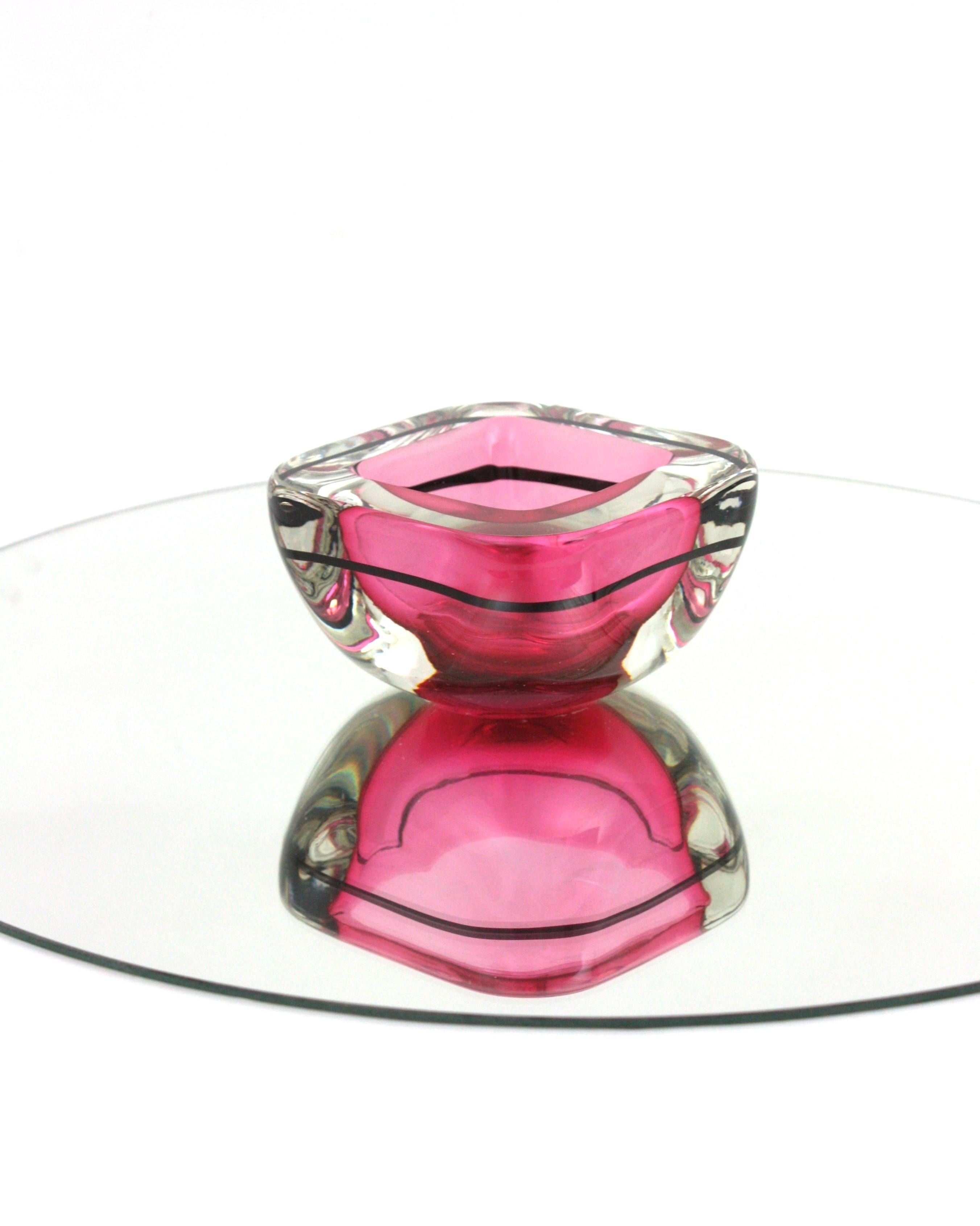 Pink Murano Glass Sommerso Geode Bowl with Black Stripe
Hand blown Murano Sommerso square shaped geode bowl in pink, black and clear glass . Italy, 1960s.
Eye-catching color in vibrant pink cased into clear glass using the 