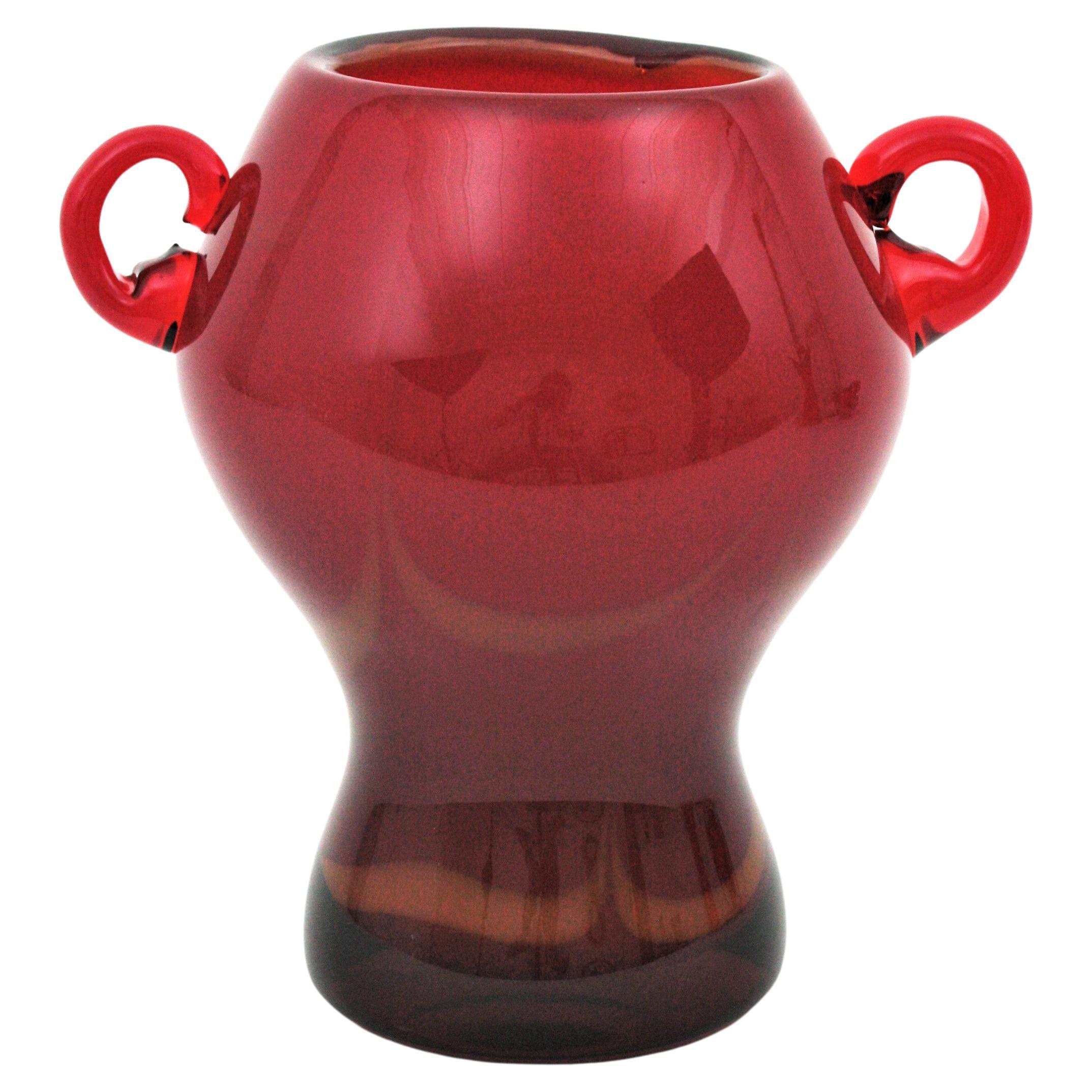 Hand blown Murano glass red vase with applied handles. Attributed to Archimede Seguso and Seguso Vetri d’Arte, Italy, 1950s.
This eye-catching Murano glass jar shaped vase is made with red glass and accented by toffee accents at the exterior part.