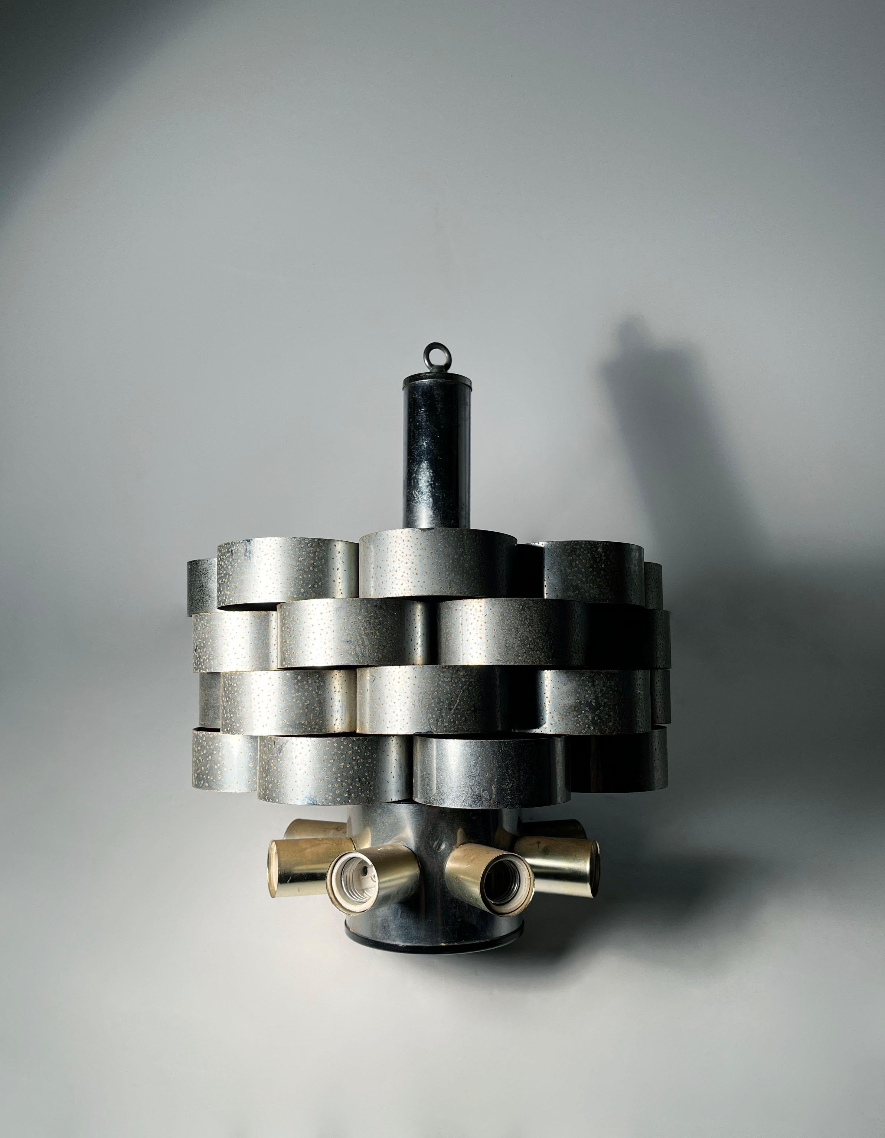 Architettonico  Lampadario a sospensione a nastro in acciaio anni '70 di Gaetano Sciolari.
Un bell'esemplare di inizio periodo. Simile al lavoro di Max Sauze.  

Alcune leggere macchie di ruggine sull'acciaio. Può desiderare di essere pulito o