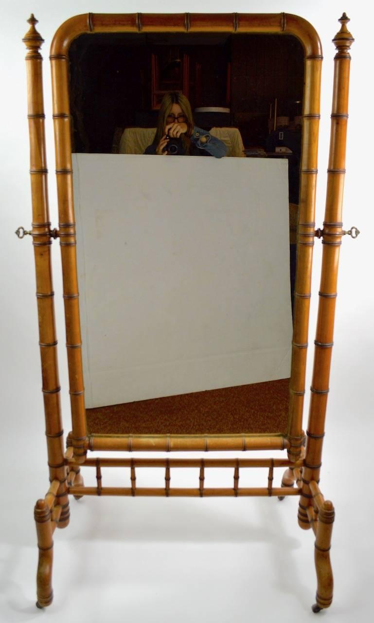 Wonderful architectural Late Victorian cheval mirror by RJ Horner. Solid turned wood faux bamboo frame with original plate glass mirror, and brass turn key hardware. The mirror will tilt to adjust position, the frame is on original brass wheel