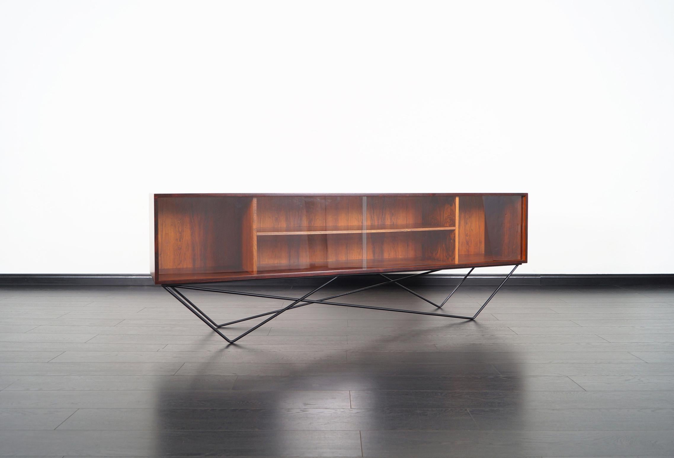 Danish modern low profile rosewood bookcase, Denmark, circa 1960s. Features two sliding glass doors, one adjustable shelf, and a stunning architectural metal base. Its versatile allows it to serve as a bookcase or credenza. Its versatile size allows