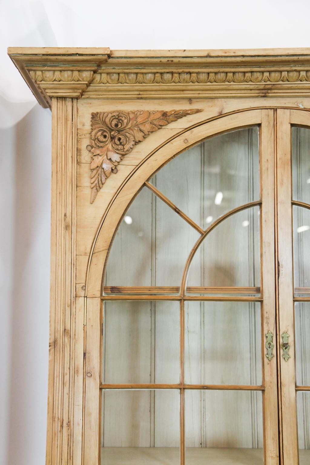 Architectural English pine breakfront, the entirety with egg and dart cornice, the outer sections with floral appliques above demilune arched glass doors, interior with adjustable shelves, two drawers above double doors below, the center section
