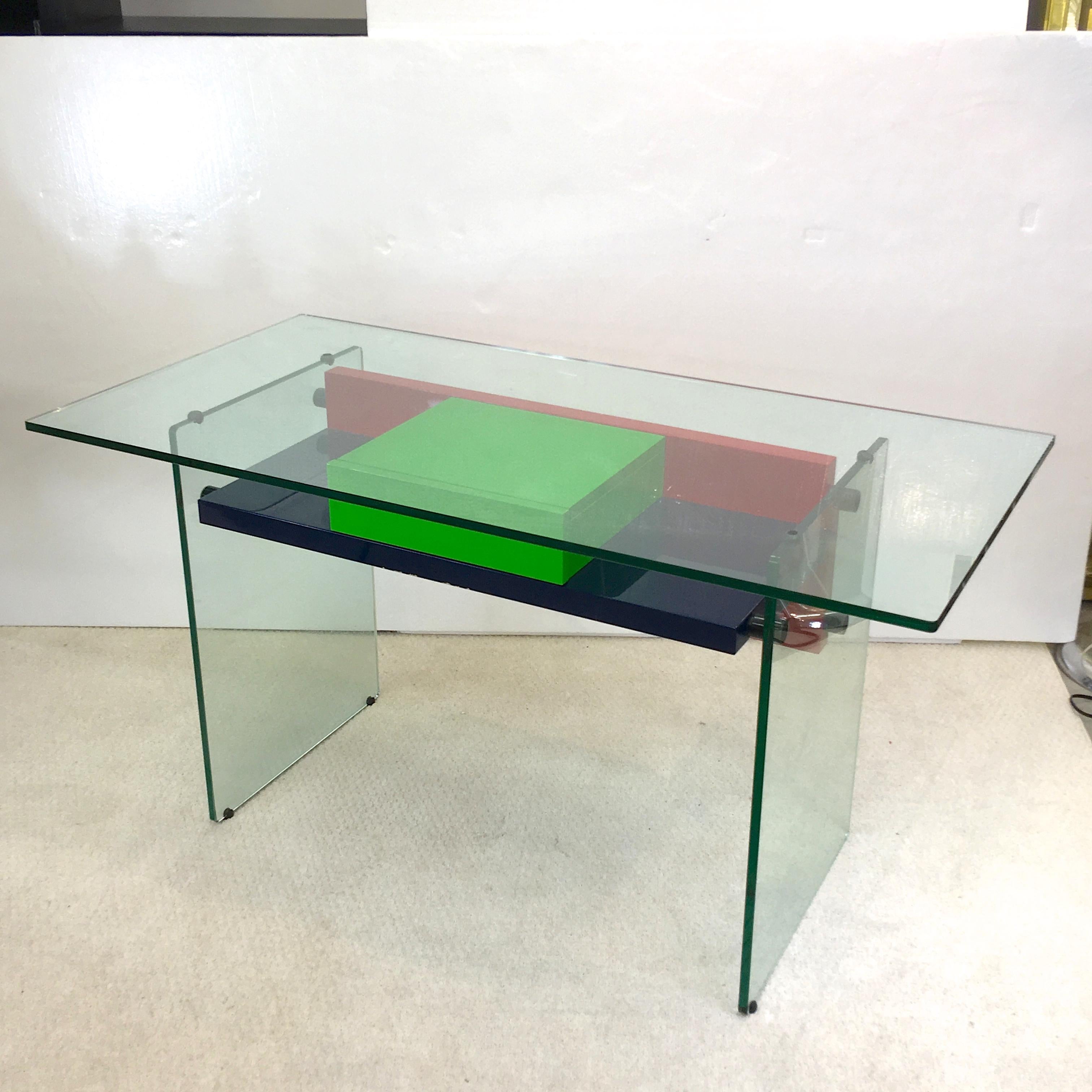 1970s French architectural desk in half inch clear tempered glass with colored high gloss lacquered wood shelf and single drawer. Navy blue, kelly green and red and blackened stainless steel glass standoffs. Kneehole height 23 inches. In the style