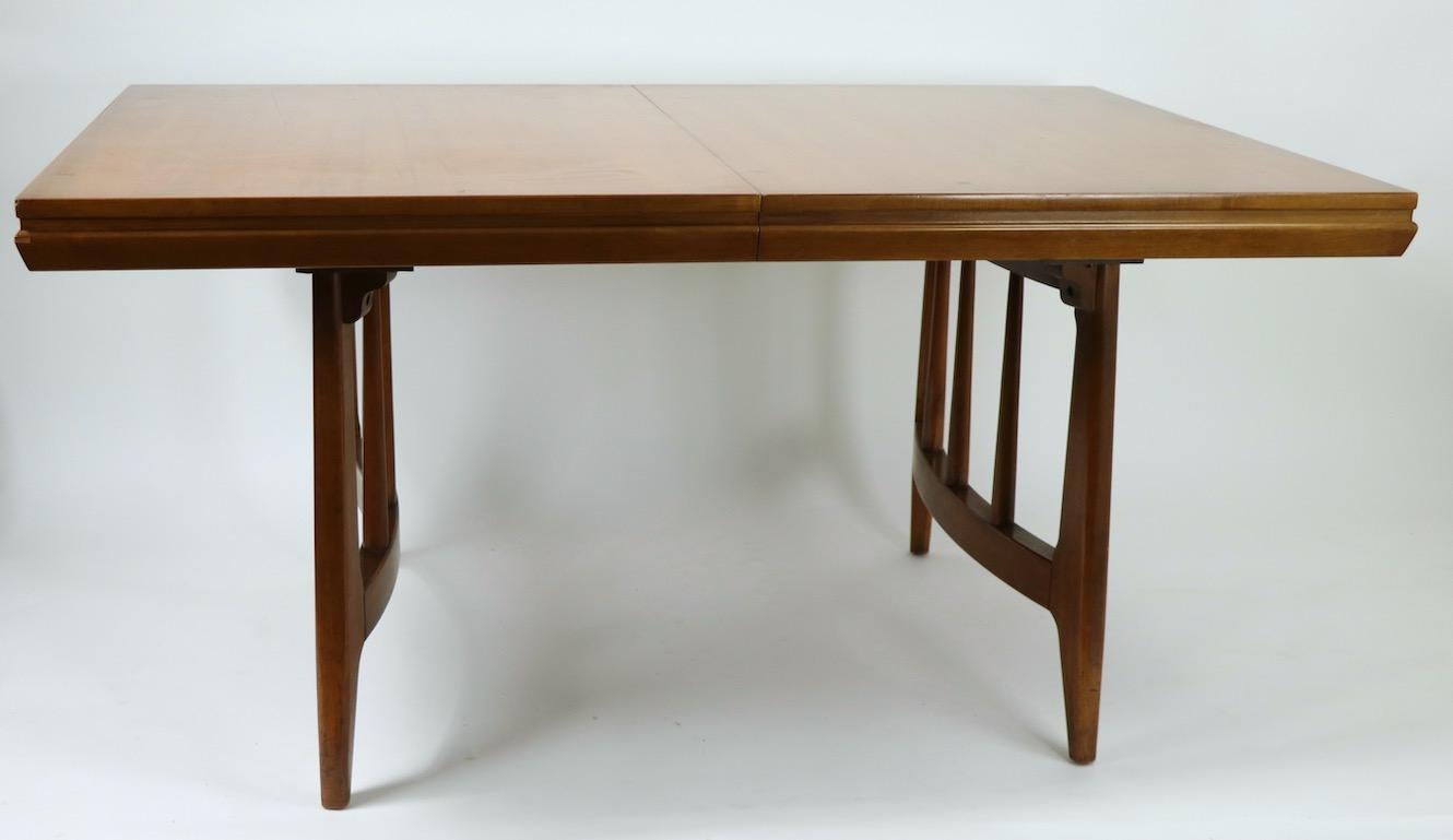 Sharp and crisp design, Mid-Century Modern dining table having opposing semi circular legs and one 12 in leaf. This example is in very fine, clean original condition, ready to use. W with leaf in place 72 in x W without leaf 60 in.