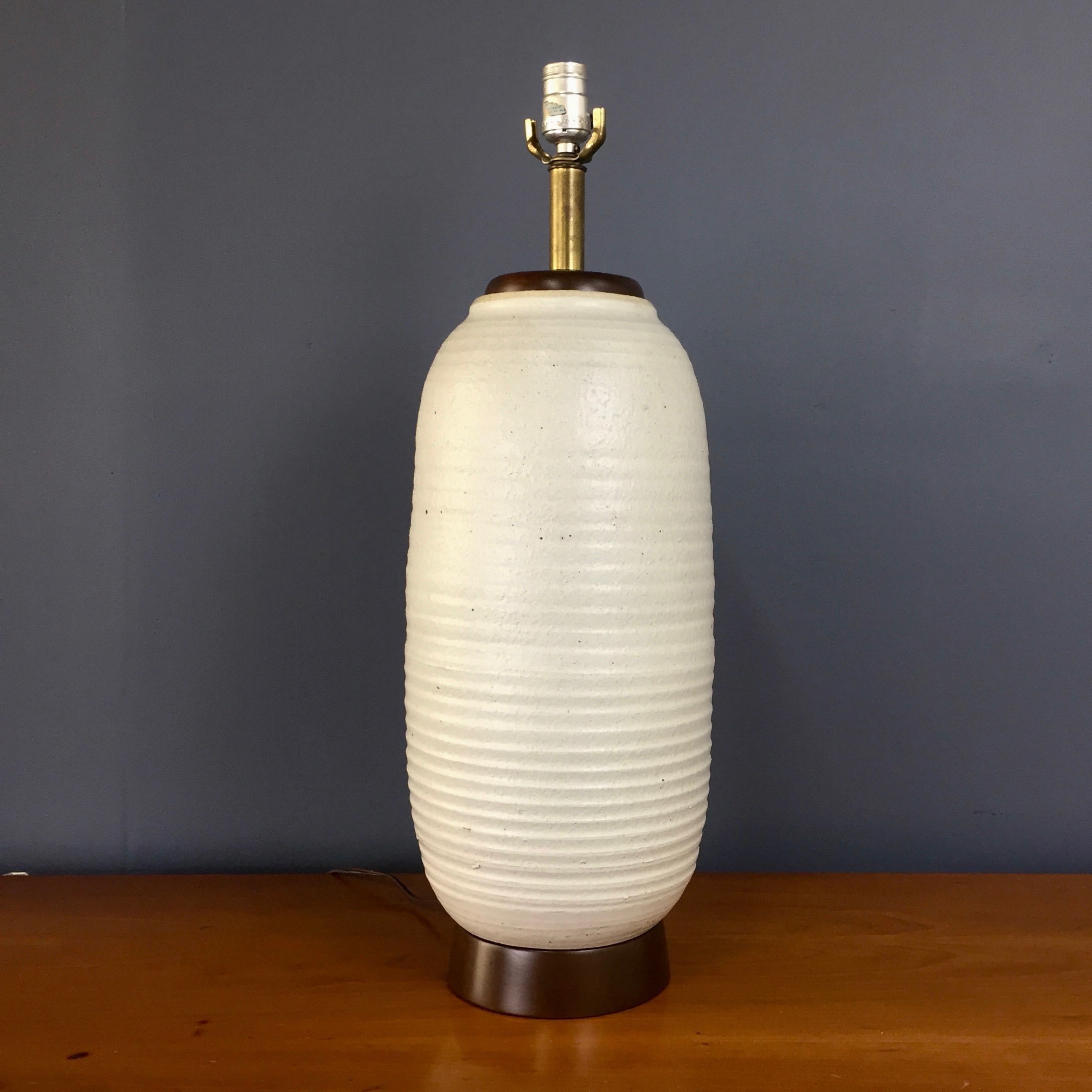 Stunning large ceramic lamp in textured oatmeal glaze with a cylindrical ribbed design. The lamp sits on a walnut plinth and has a walnut cap. this lamp has been rewired and the walnut has been refinished.