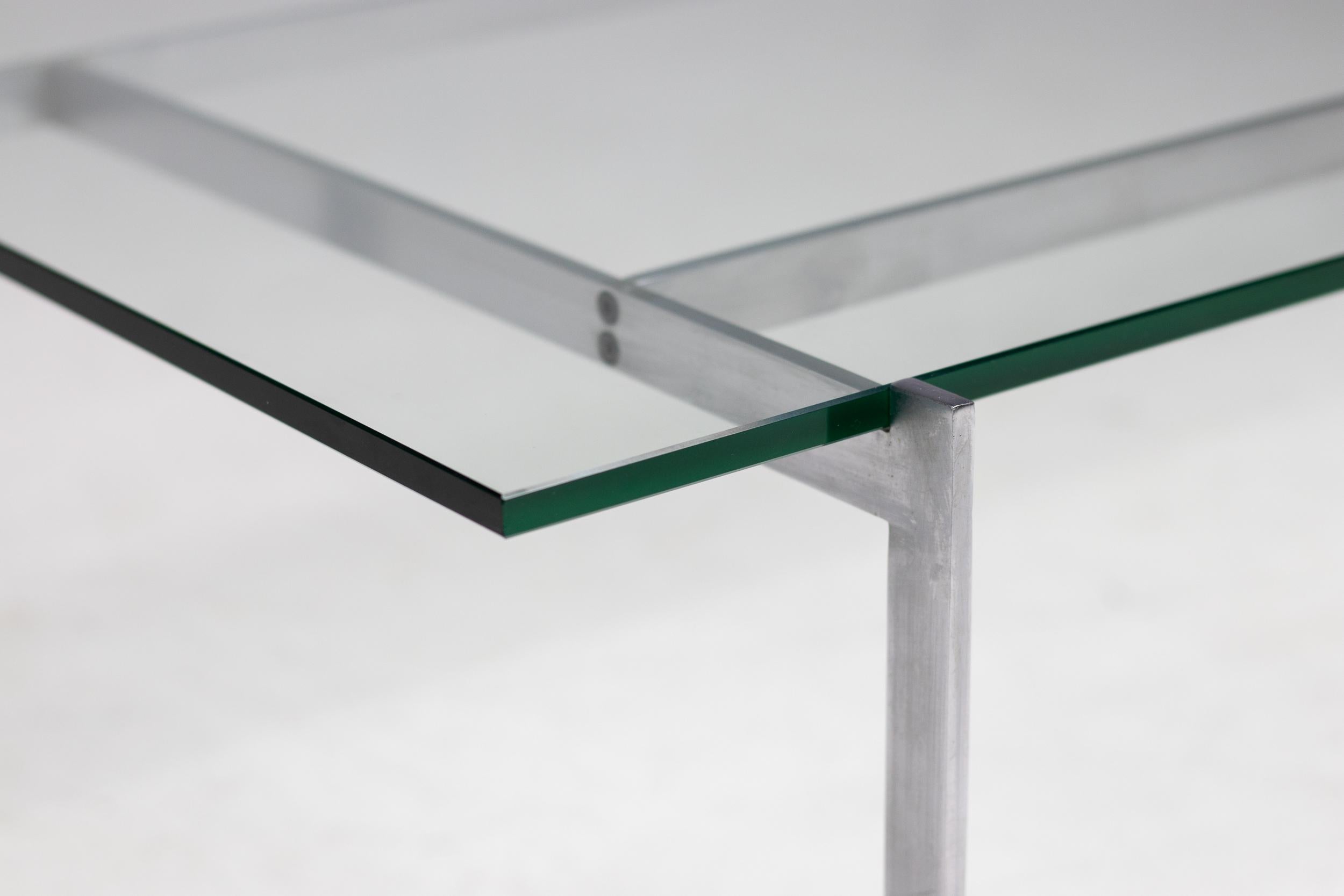 This table is the epitome of minimalistic yet monumental design. The asymmetrical shaped matte chrome steel frame holds a glass top. With this table the designer was able to get the architectural core in his design. 
The table, by means of the steel