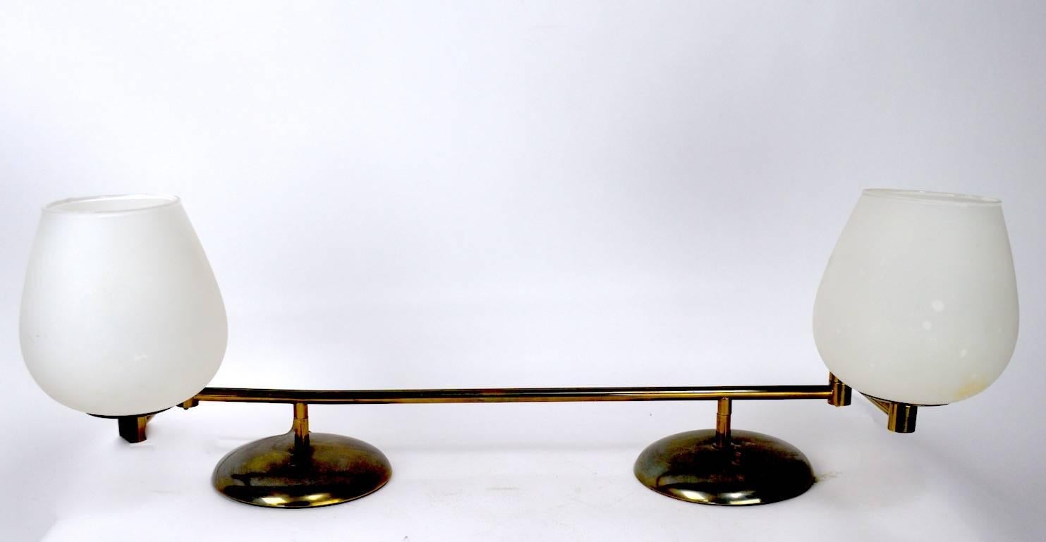 Interesting two-light swing arm desk or table lamp. Brass structure supports frosted glass globes, each has independent on/off function, each arm is 7 inches L. Total L of lamp in extended position 40 inches. Manufacture attributed to Nessen Studio.