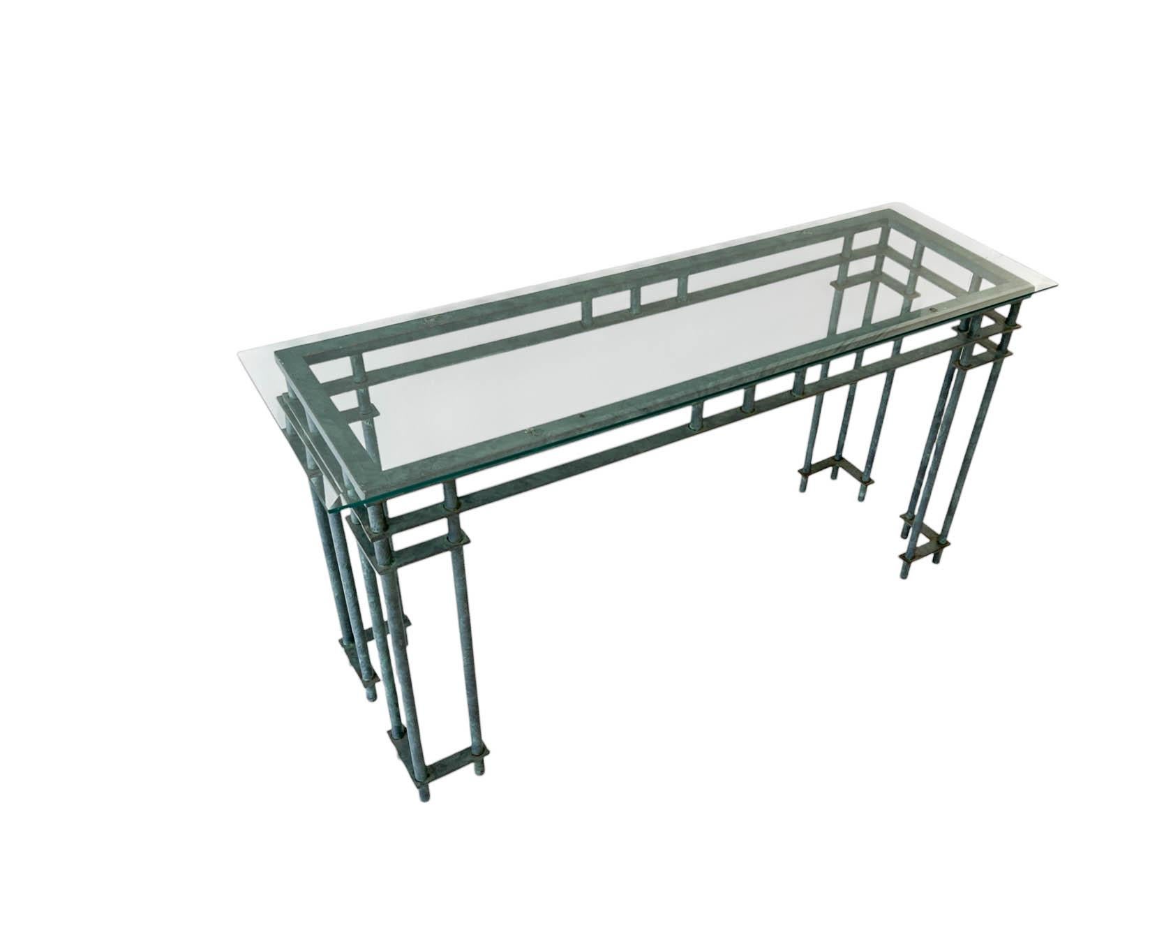 Cette table console, fabriquée en fer forgé avec une finition magnifiquement patinée, incarne la fusion des sensibilités du design Art déco et industriel. Les lignes architecturales de sa base sont constituées d'une série de tiges verticales
