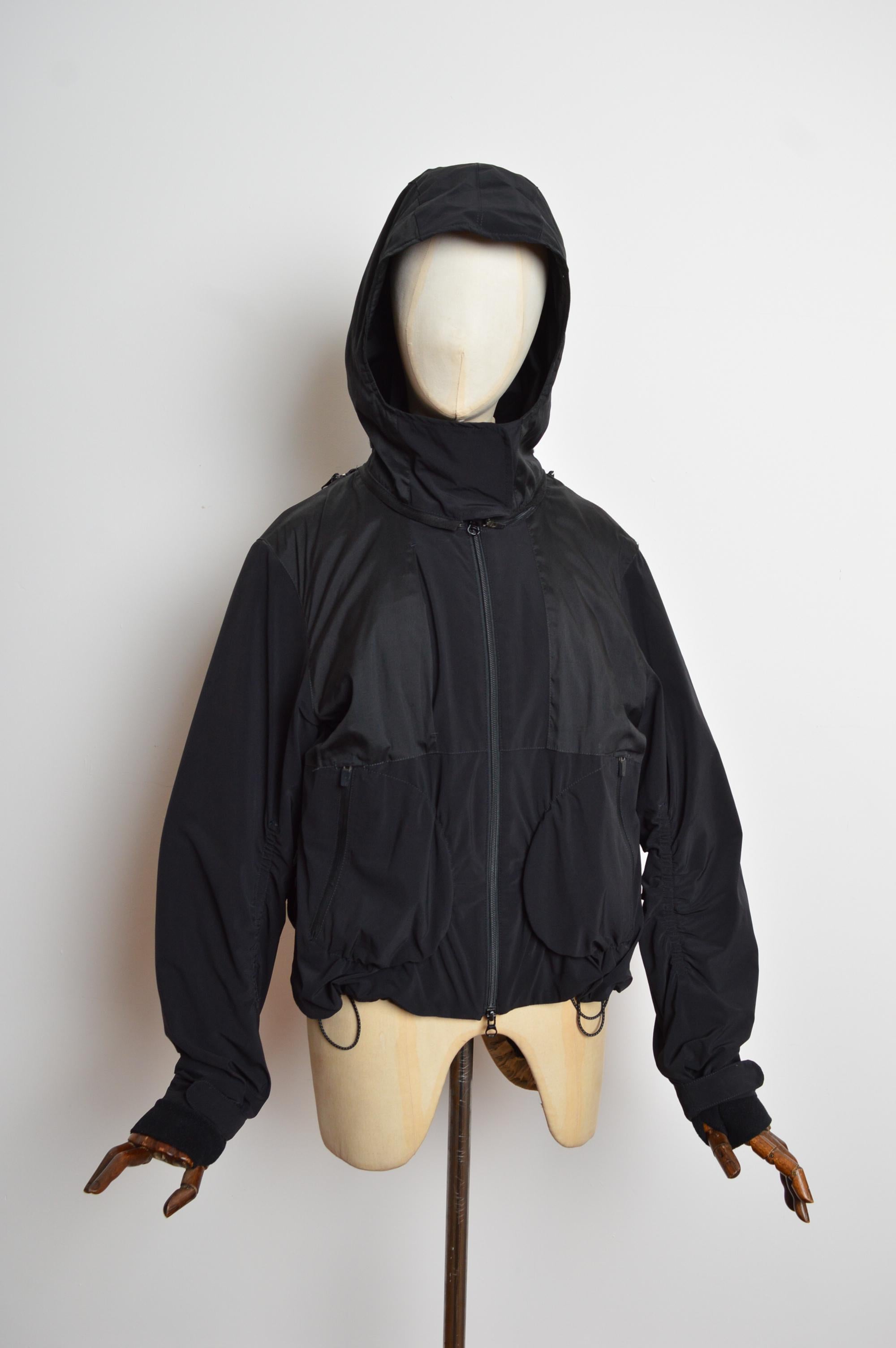  Archival Marithé François Girbaud Technical Backpack Transformable Cagoule Nylon Black Jacket.
The Coat features a variety of technical details such as adjustable draw ties at the waist, Hidden front Pockets, fleece mittens, fold away Hood that can