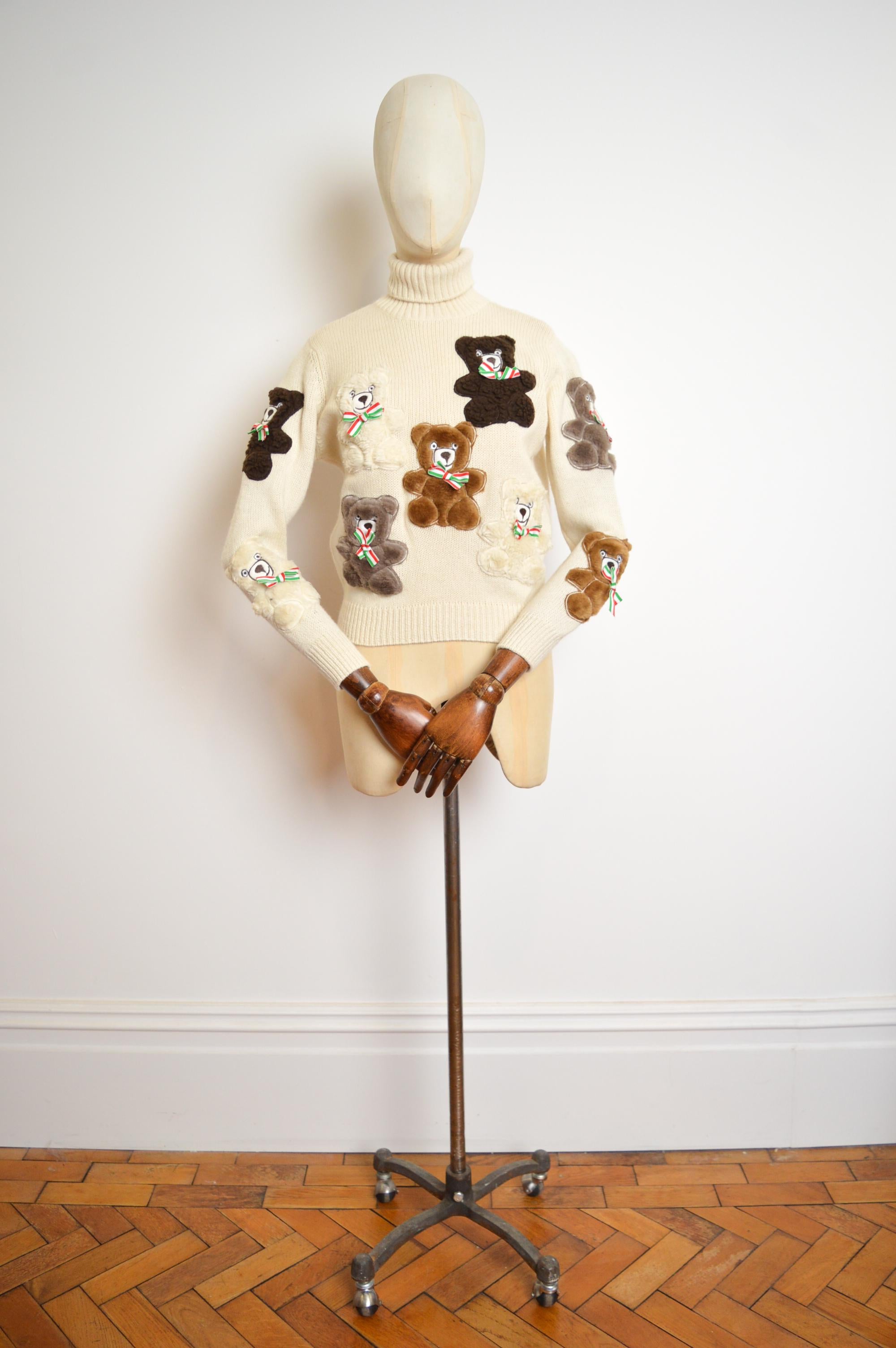 Rare Archival 1990's Teddy Bear sweater designer by Franco Moschino for Moschino's 'Couture' line.
Beautiful Soft Cream roll neck sweater with a variety of Fluffy hand sewn ornate teddy bear appliqués with Italian flag coloured ribbon neck bows.