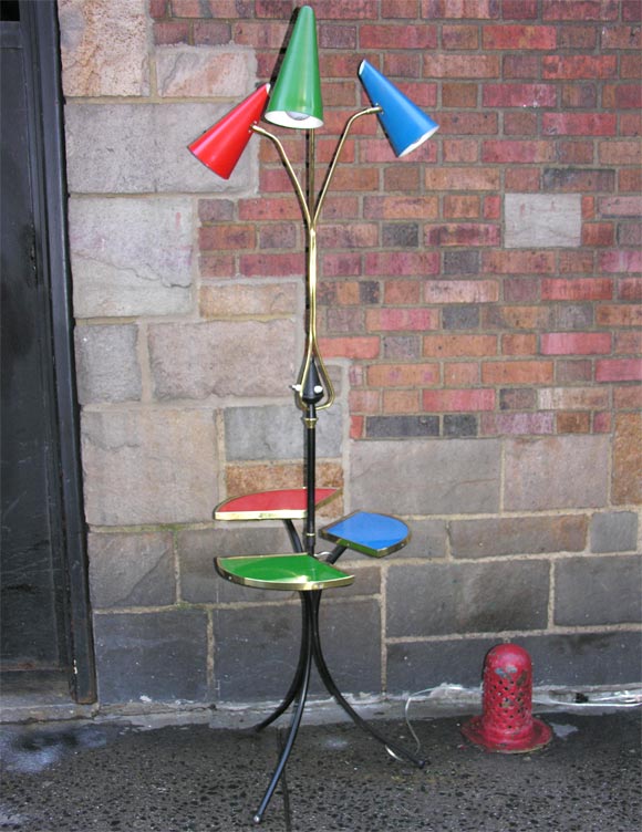 An Italian floor lamp by Stilnovo, produced circa 1950s with three pivoting conical shades in red, green and blue, supported by curved brass stems, above three-tiered shelves with matching reverse painted glass tops, mounted on black enamel tripod