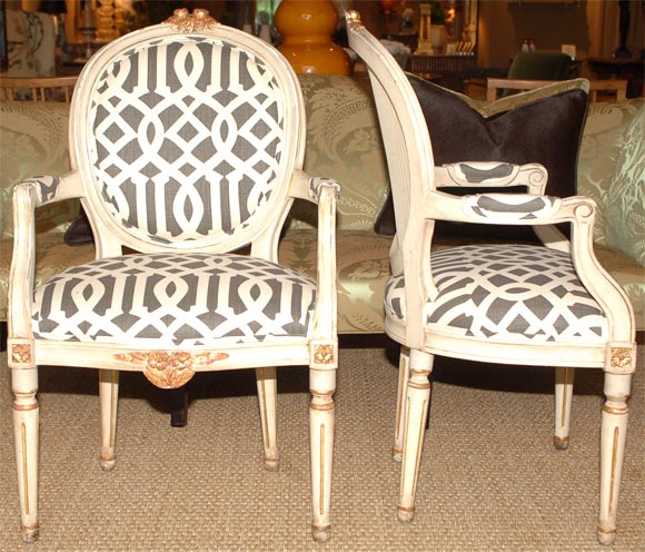 In the Louis XVI Taste, a very unique pair of Gustavian armchairs. Cream paint and parcel gilt oval back with gilded rosette detail resting on tapering fluted legs. Handsomely upholstered in Linen Lattice in black and white knife edge tape with back