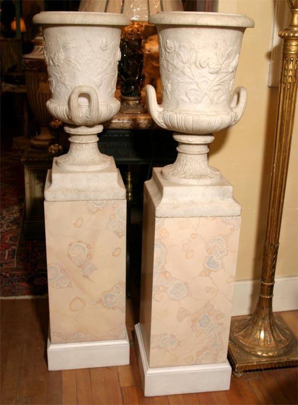 A pair of carved white granite classical urns with floral decoration on the bodies. Custom-made marbleized wood pedestals.

Measure: urns are 26.5 tall 14 diameter 

pedestals 29 tall.