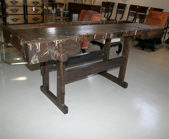 Massive dark patinated worksurface has all-wooden vices at either end, supported on original trestle base, stamped with the original owner's name. Signed on metal mounts. Beautiful overall coloration of aged wood, paint spots, burns and tool scars,